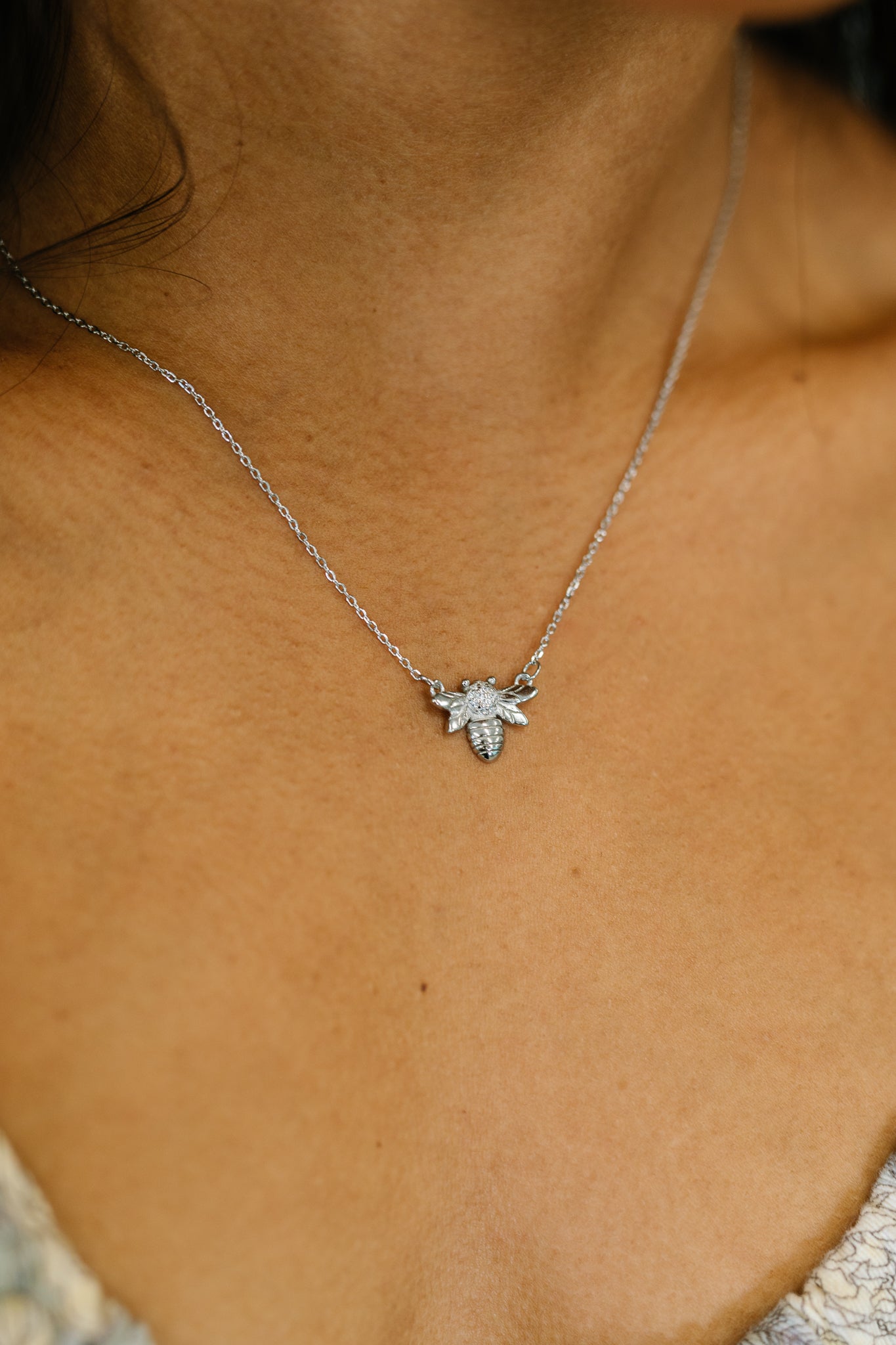 Delicate silver bee pendant necklace with sparkling zirconia stones worn on a slender chain in an eclectic style