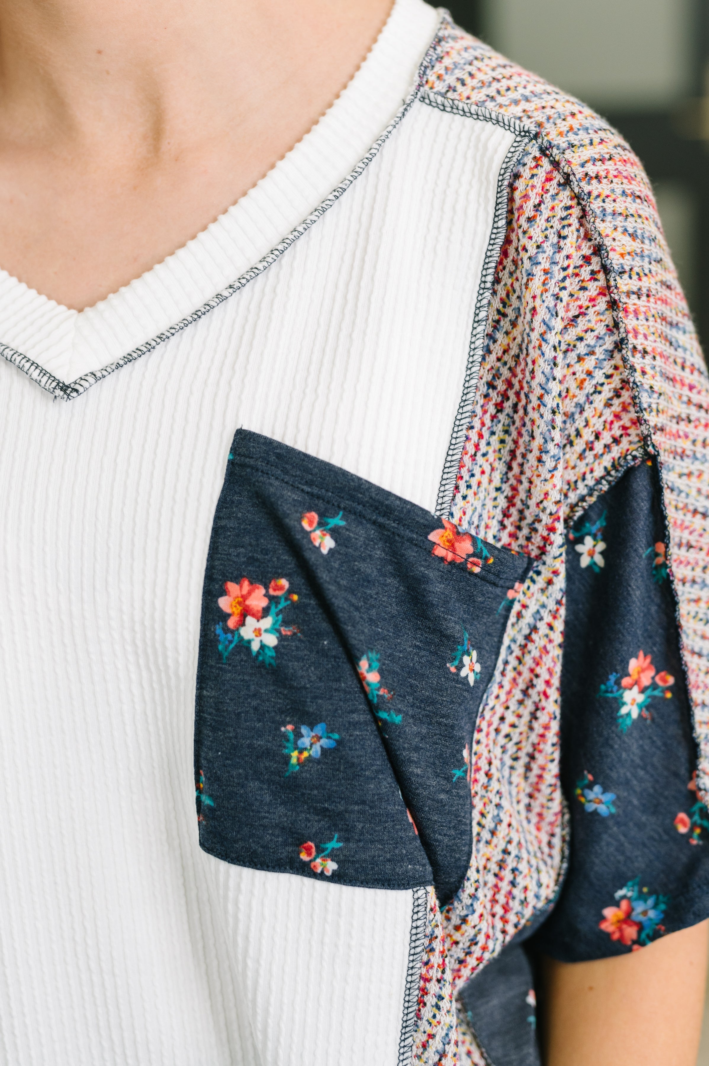 Close-up of navy floral pocket and sleeve detail on textured cream knit top with multicolor woven panel accents