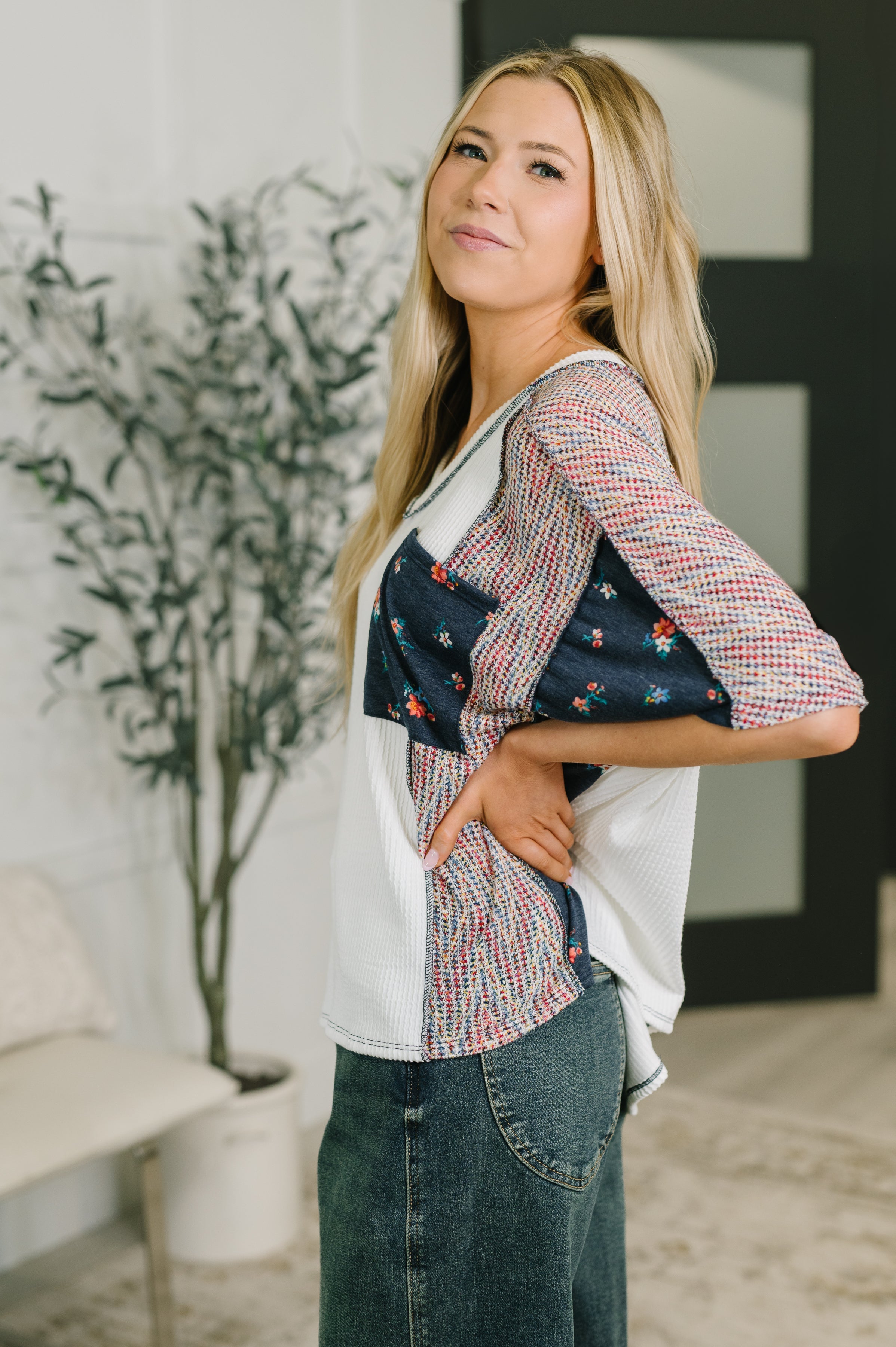 Side view of woman wearing relaxed fit top with color block and floral patterns paired with blue denim skirt indoors