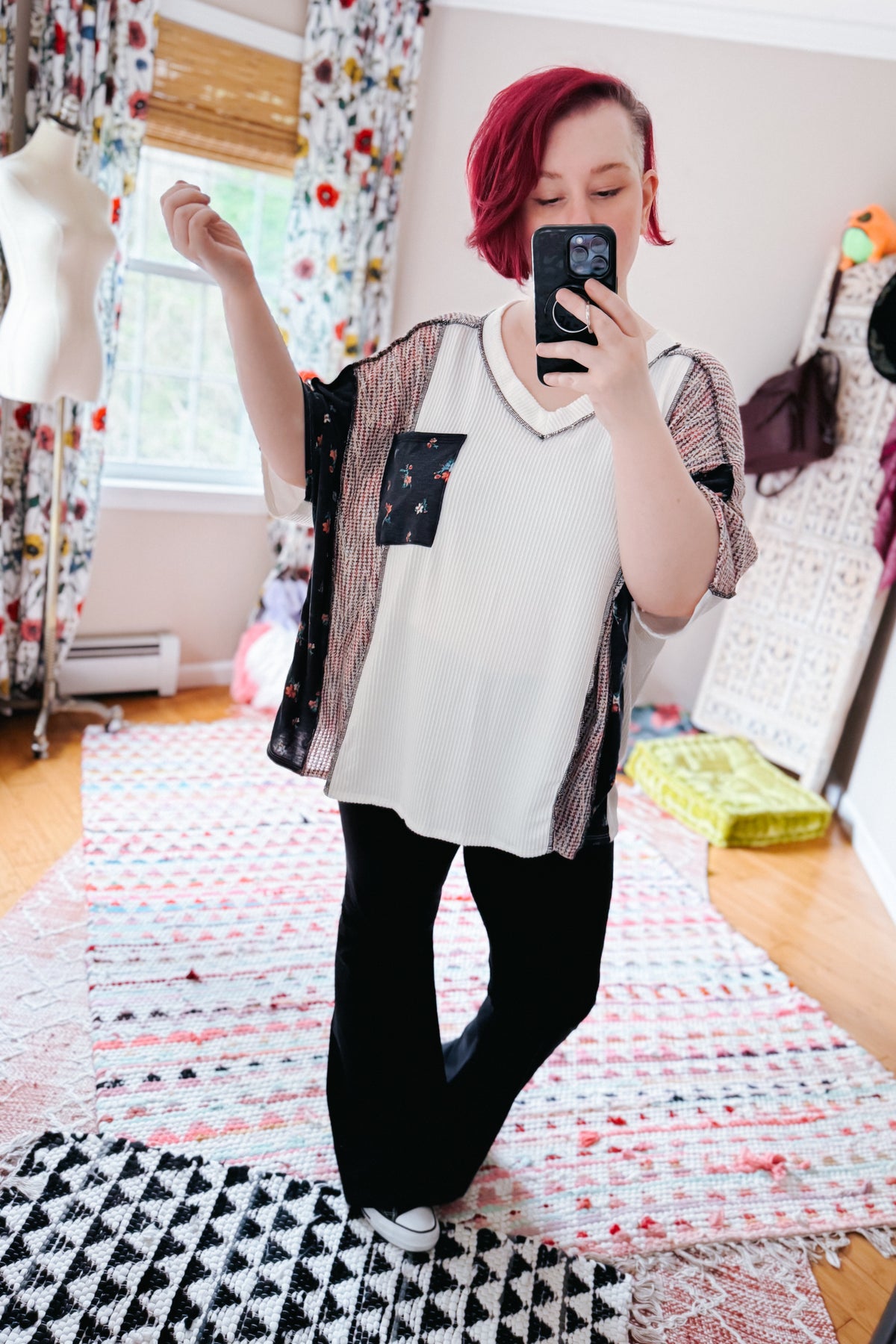 Woman taking a mirror selfie in a navy and cream color block knit top with black pants in a colorful bedroom
