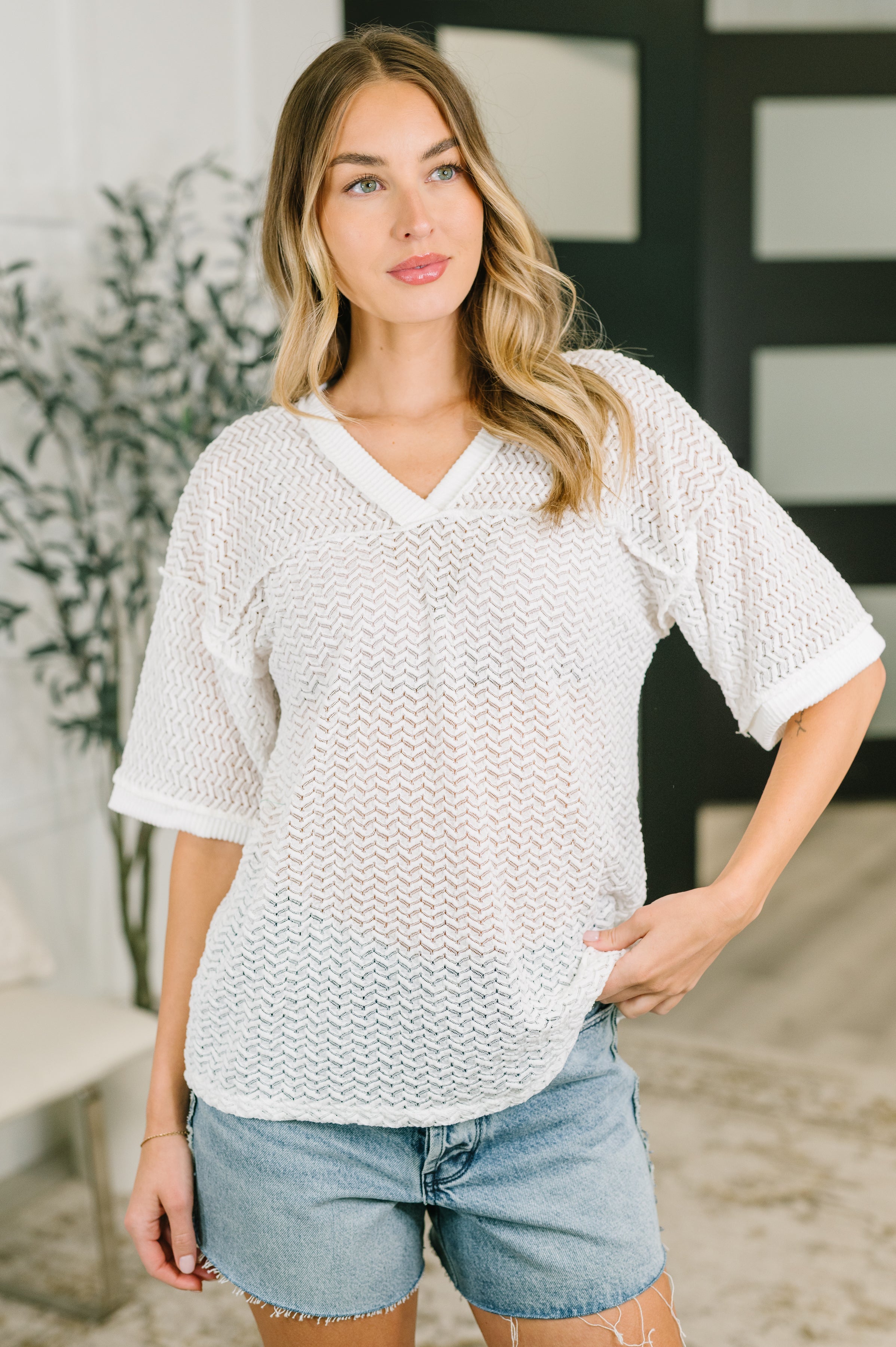 Woman wearing cream textured oversized top with V-neck and drop shoulders paired with light denim shorts indoors