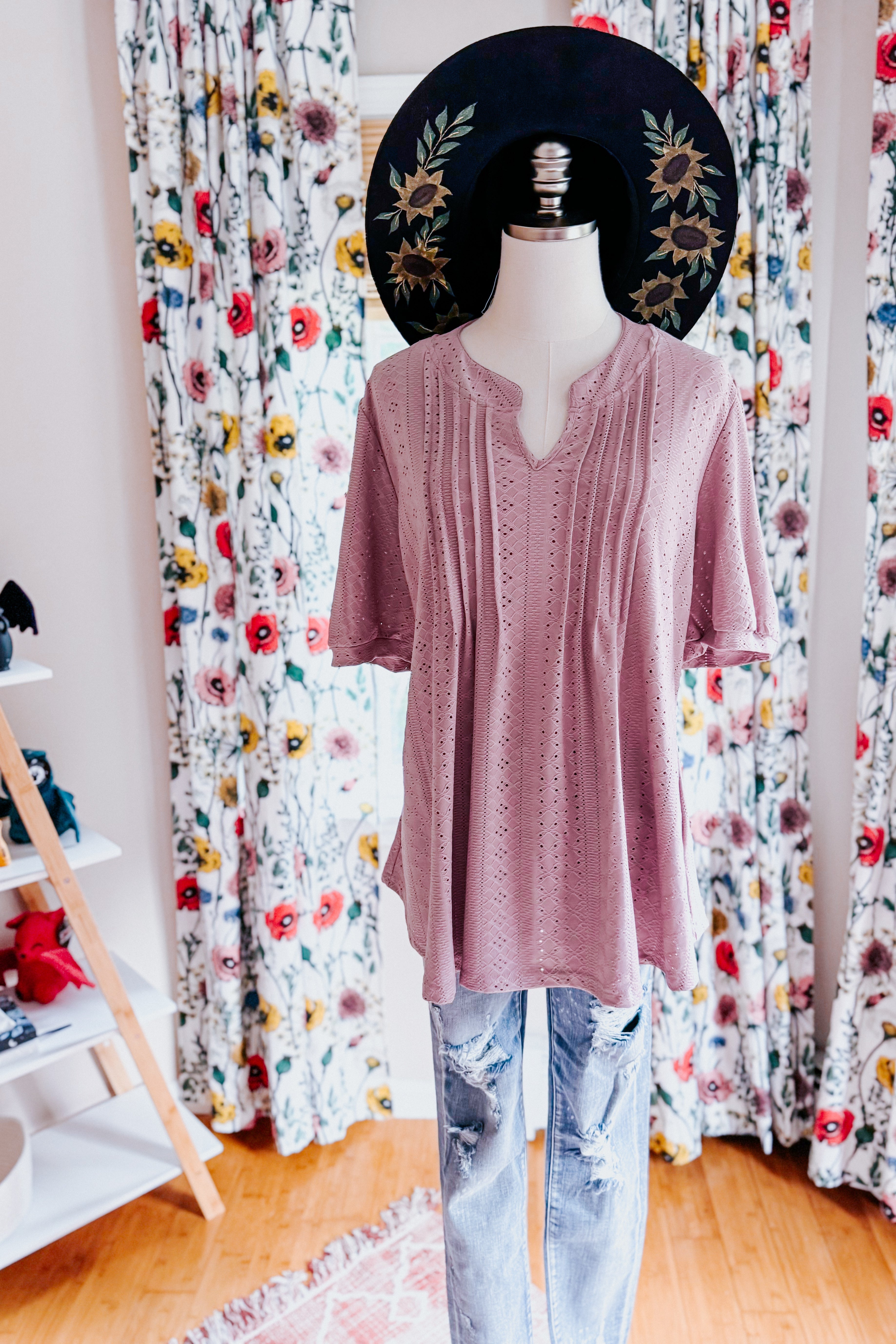 Light mauve pleated front blouse with textured fabric displayed on mannequin with floral curtains and distressed jeans