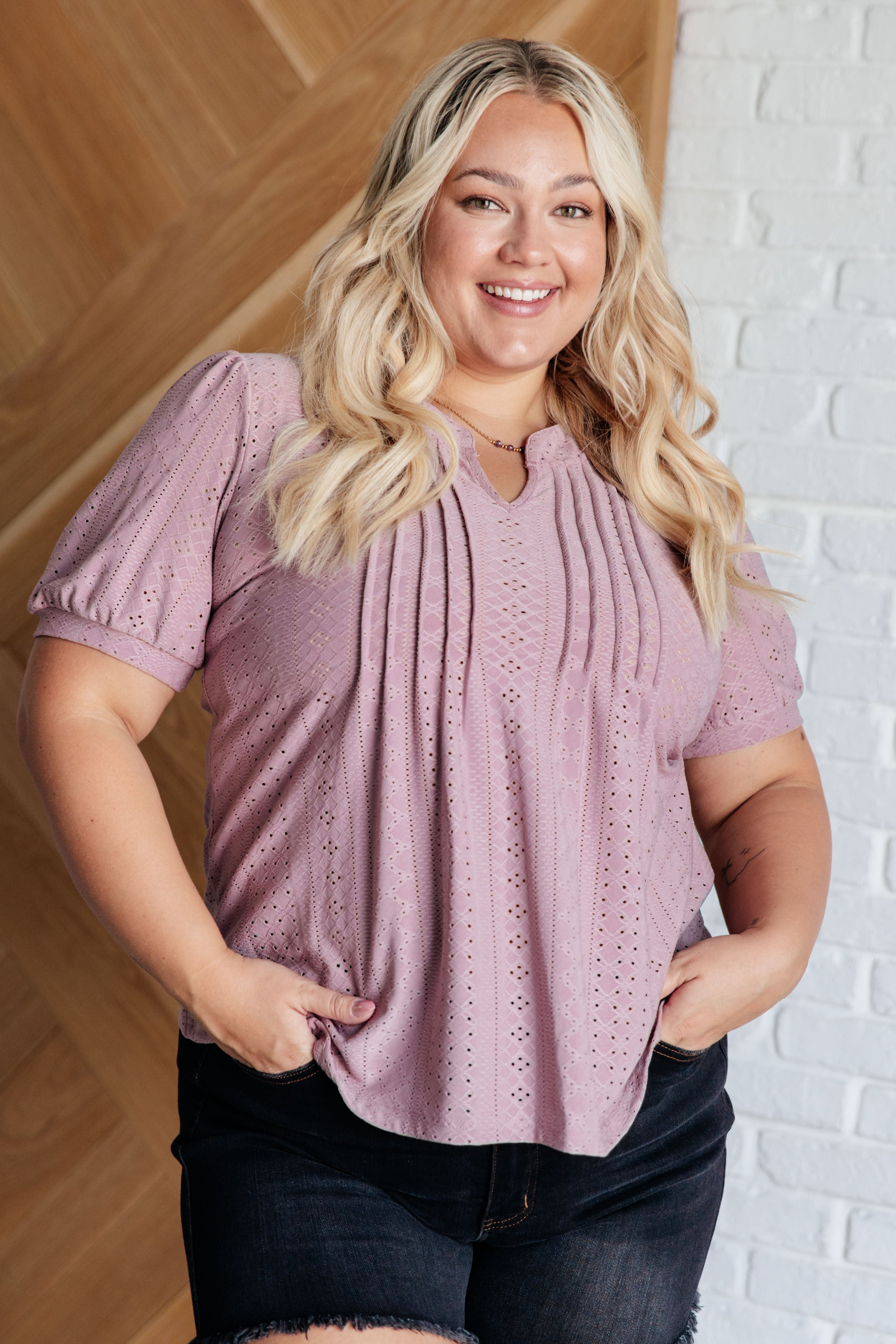 Curvy woman wearing dusty mauve eyelet blouse with pintuck pleats and short puff sleeves paired with black shorts