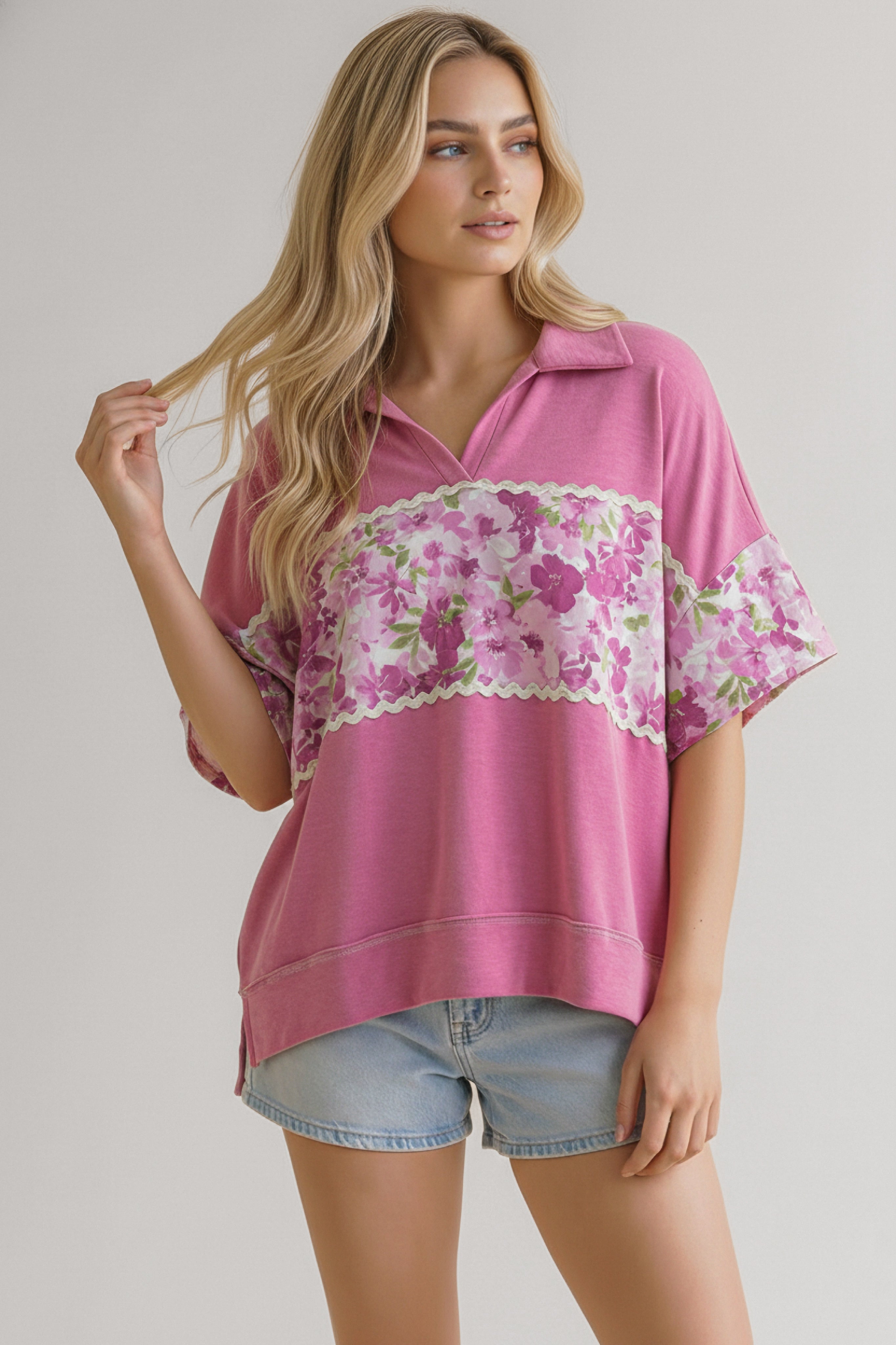 Woman wearing a loose pink top with floral band across chest and sleeves paired with light denim shorts