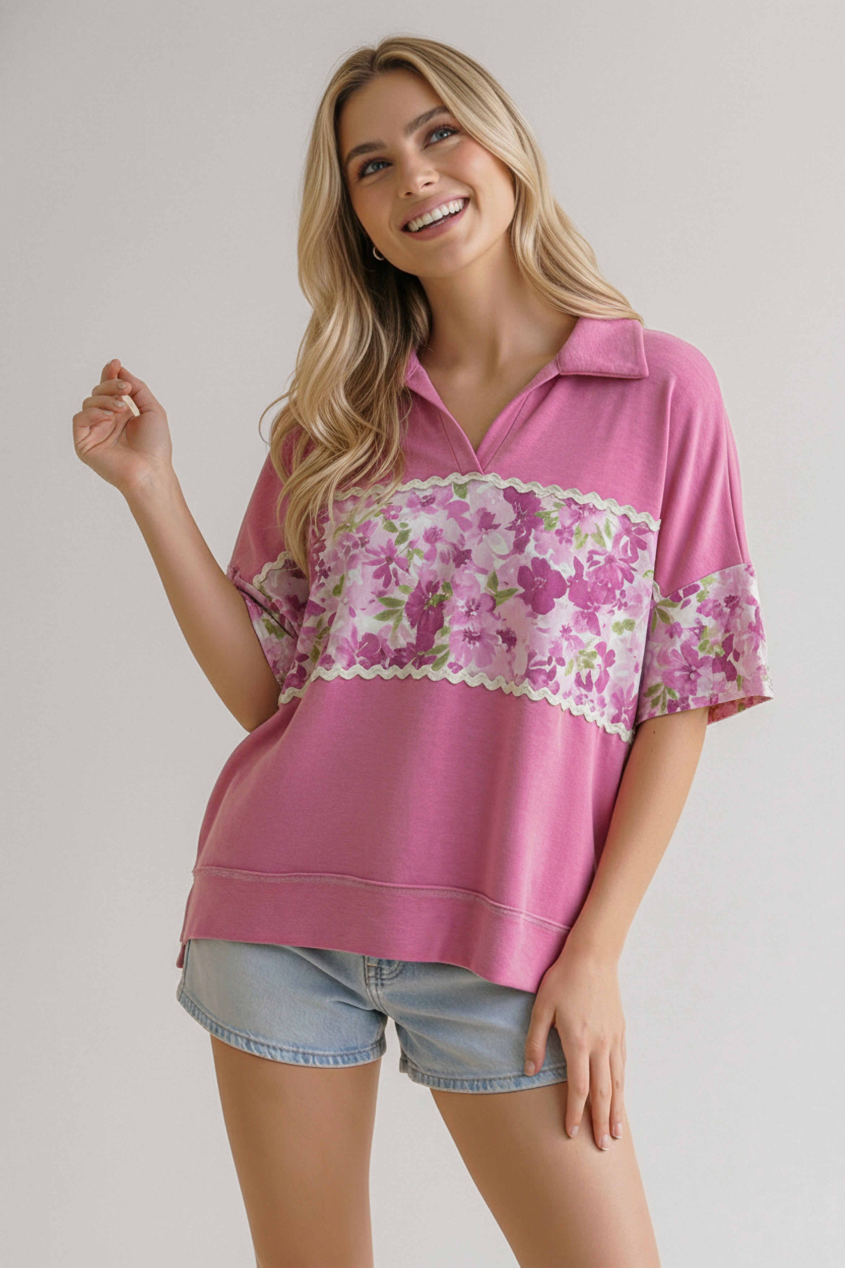 Smiling woman wearing a pink collared top with floral band across chest and sleeves paired with light denim shorts