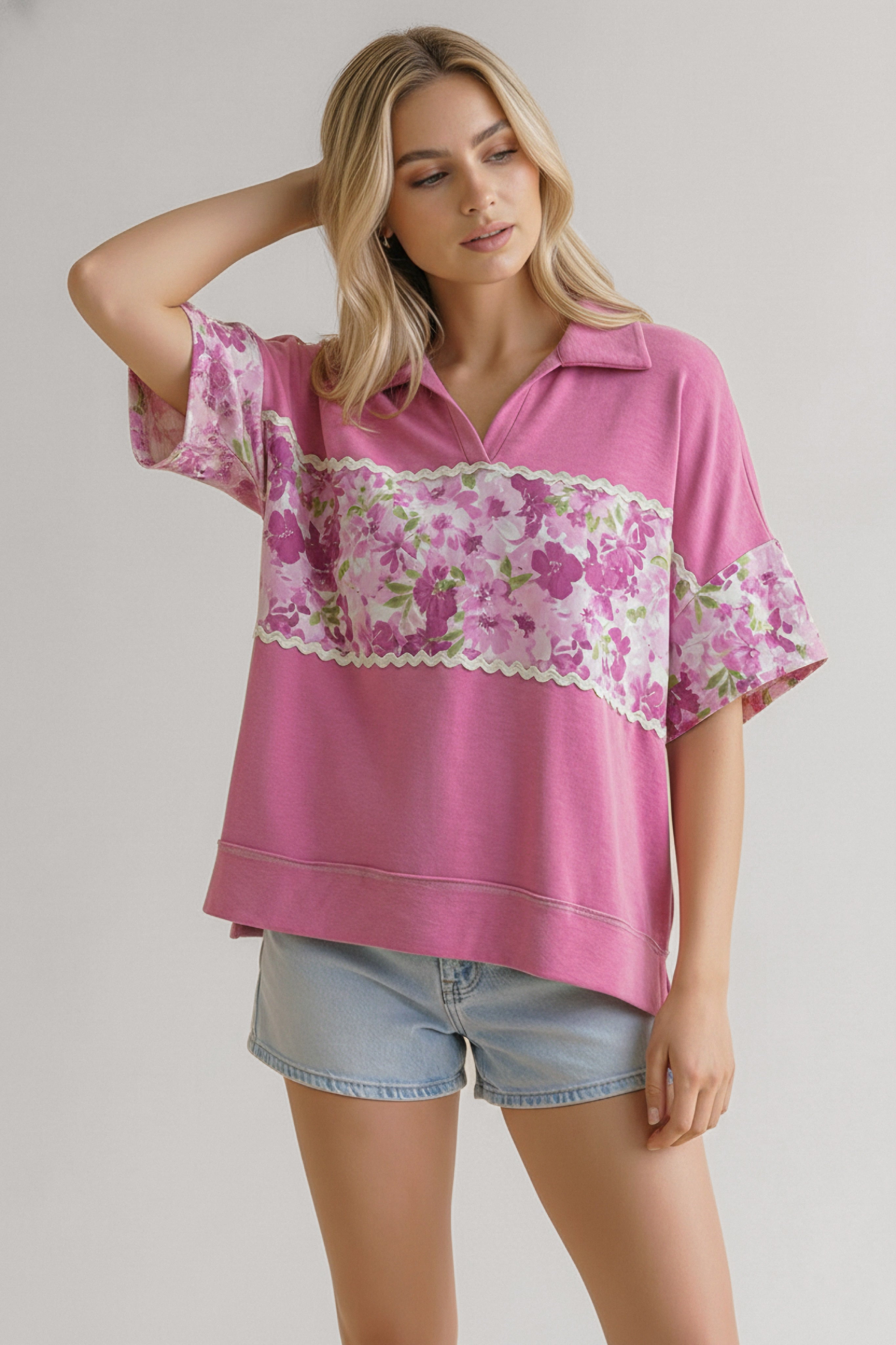 Woman wearing a pink short-sleeve top with floral panels and collar paired with light denim shorts