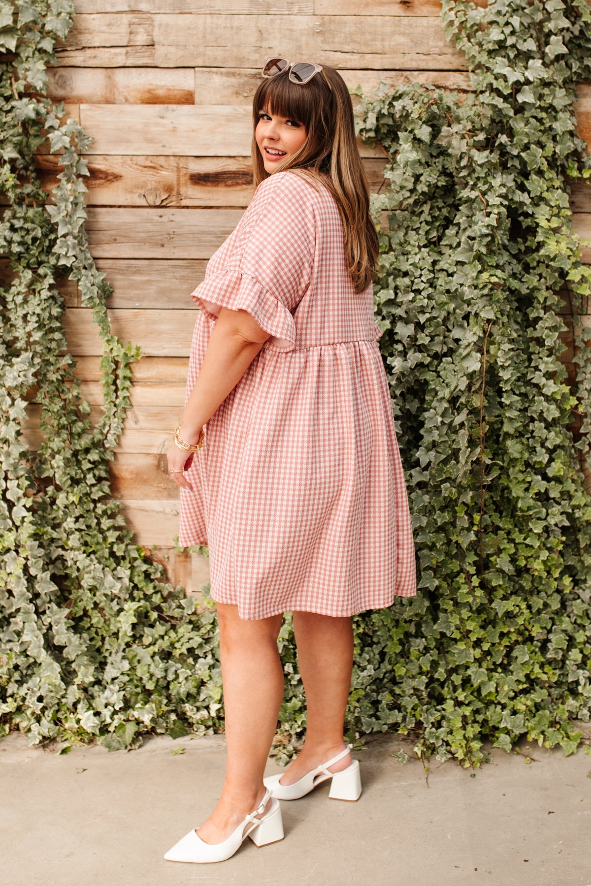 Curvy woman wearing pink gingham short sleeve dress with ruffle detail and white block heel shoes outdoors