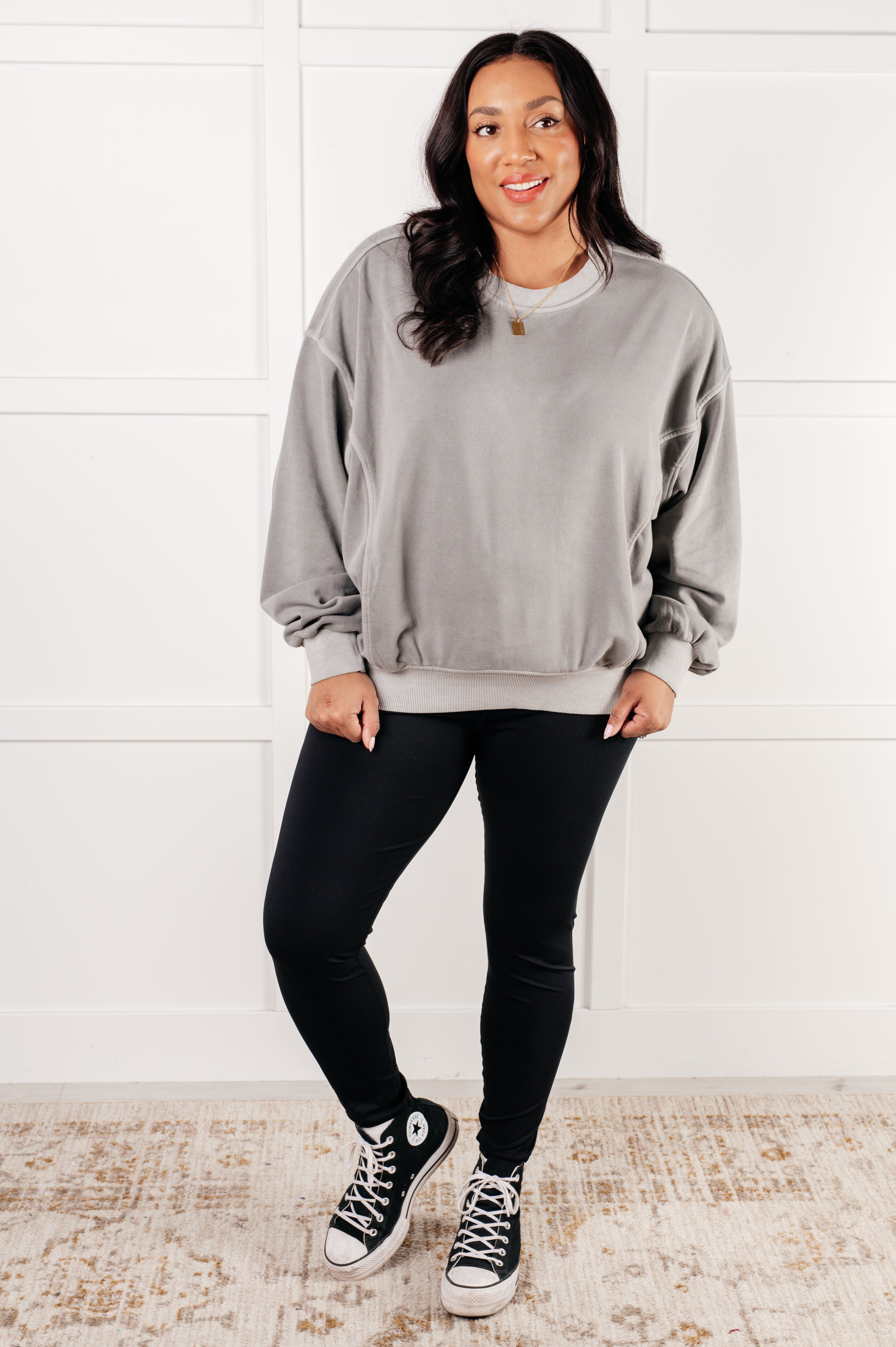 Woman wearing loose gray Beyond the Basics Pullover and black leggings paired with black high-top sneakers indoors