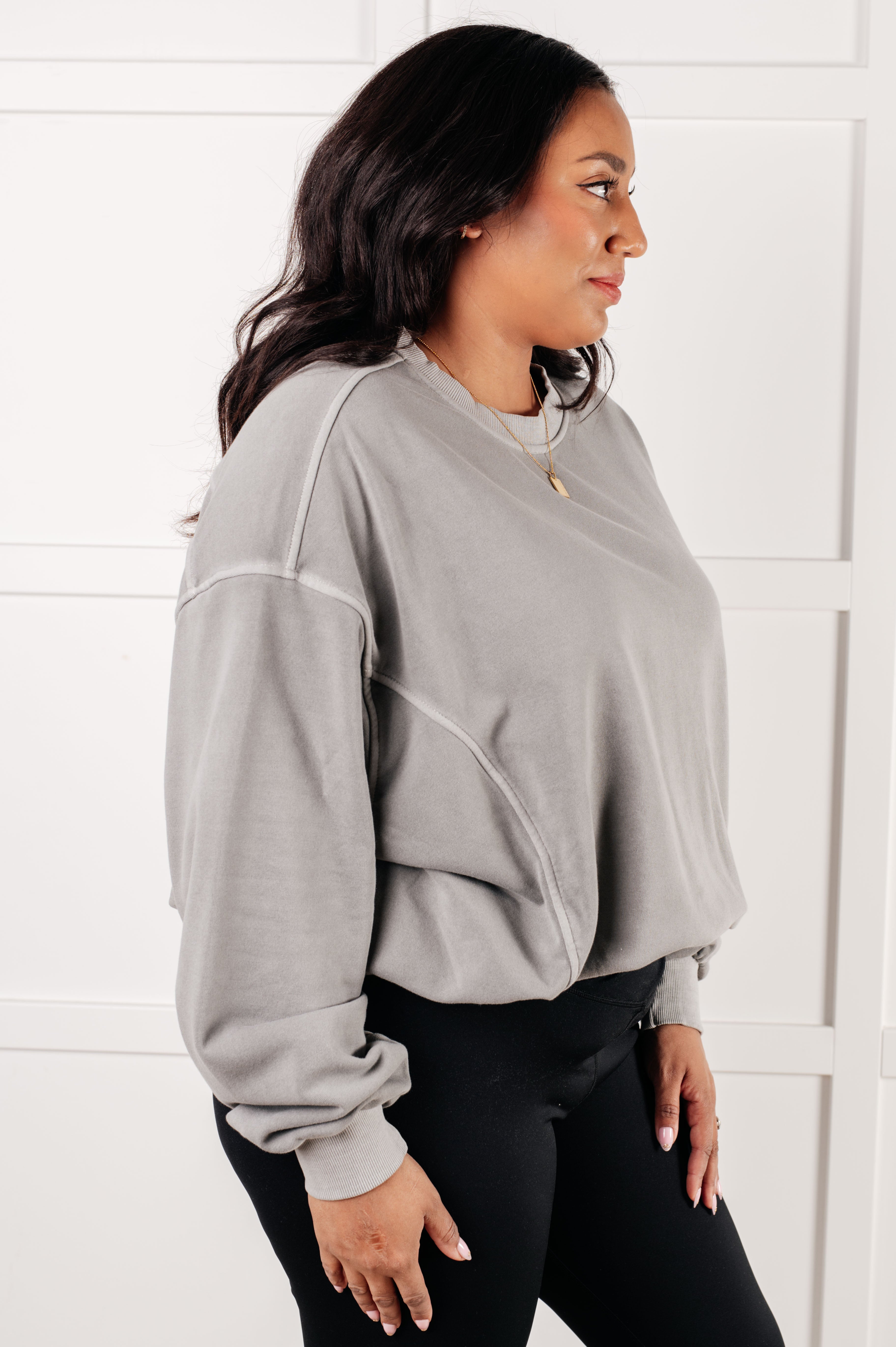 Woman wearing loose fit light gray Beyond the Basics Pullover with black fitted leggings against white paneled wall