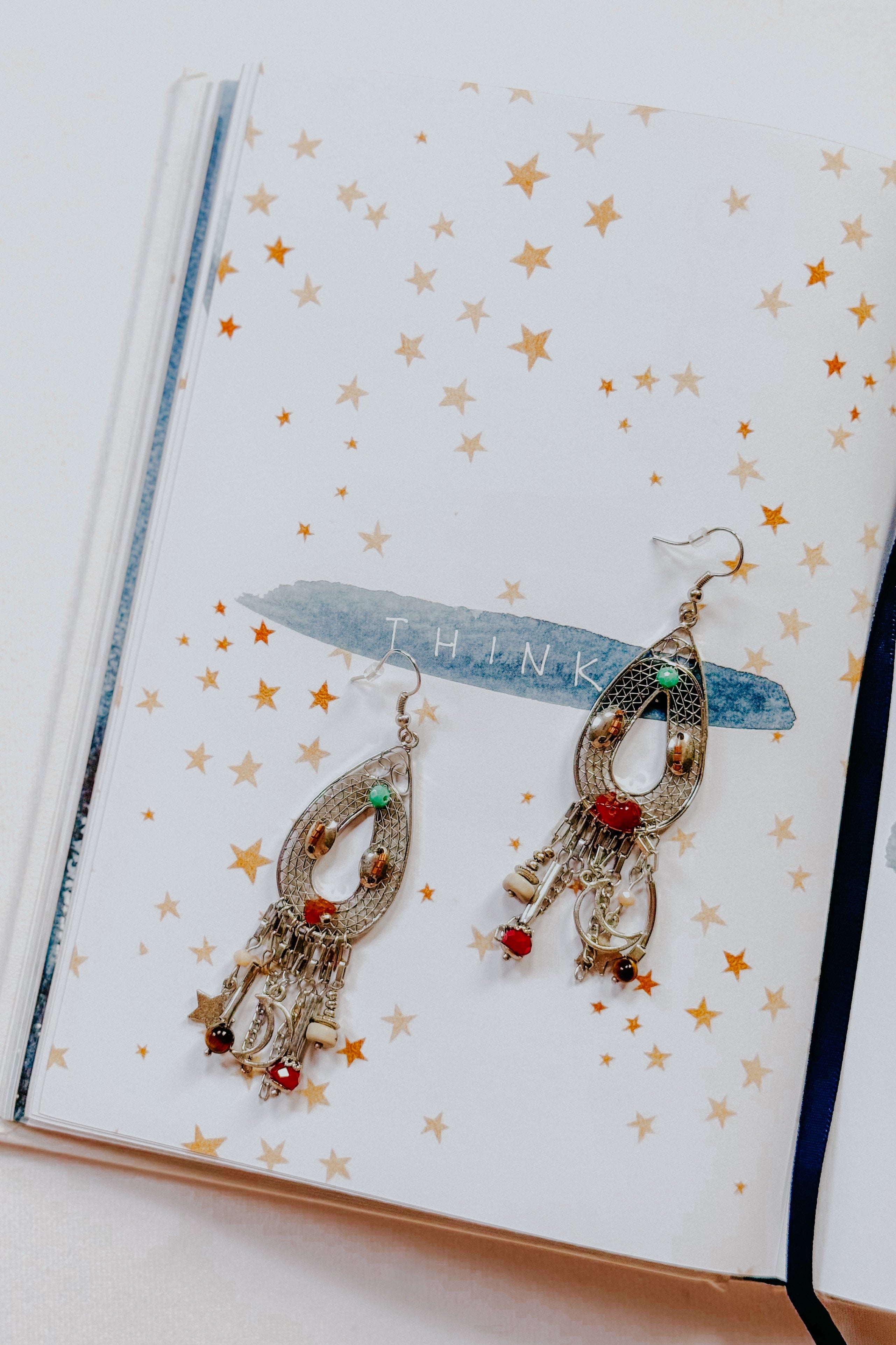 Silver teardrop earrings with beads, charms including moon and star details on an open notebook page with stars design