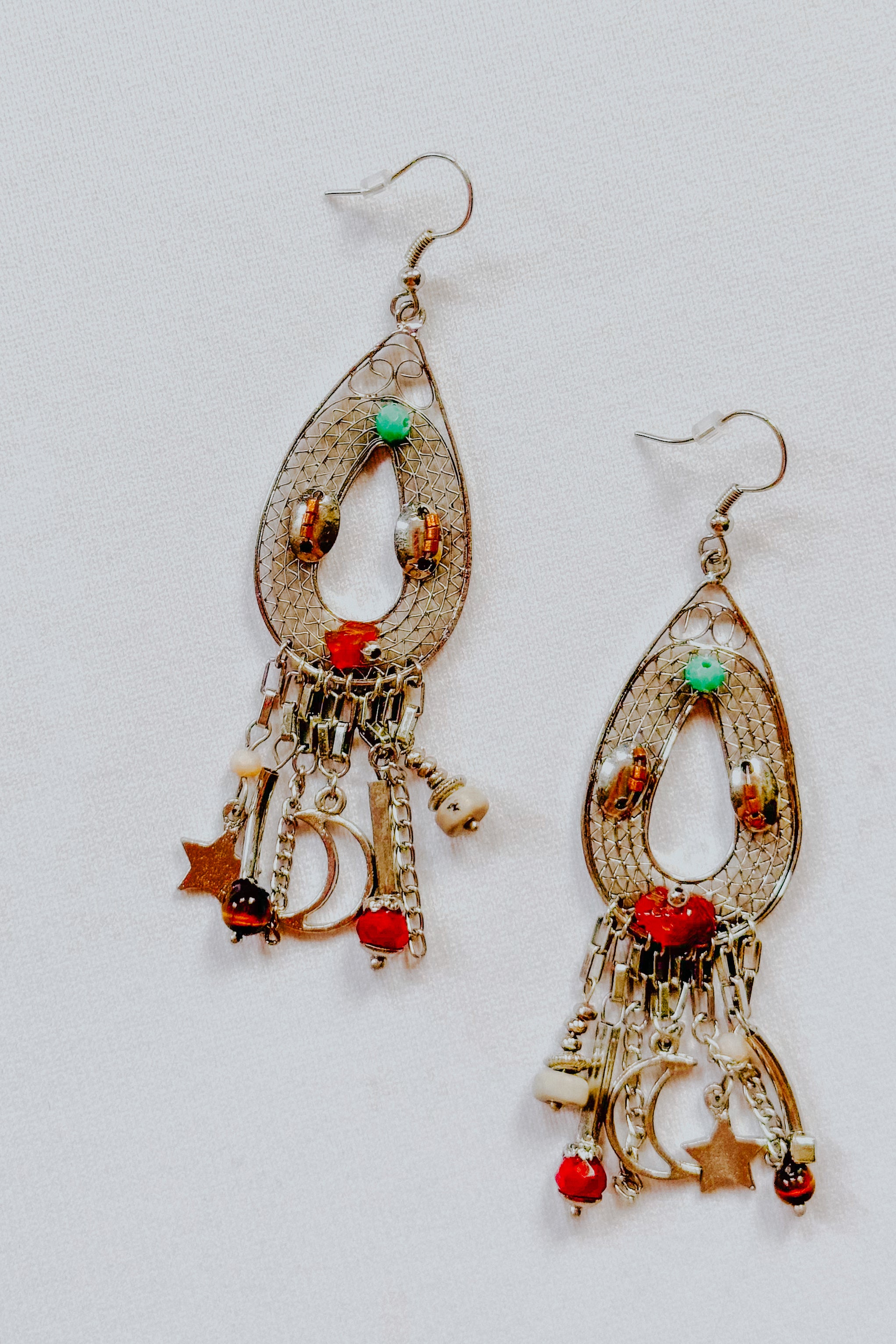Silver teardrop earrings with moon, star charms, and red, turquoise, and brown beads on intricate filigree wire design