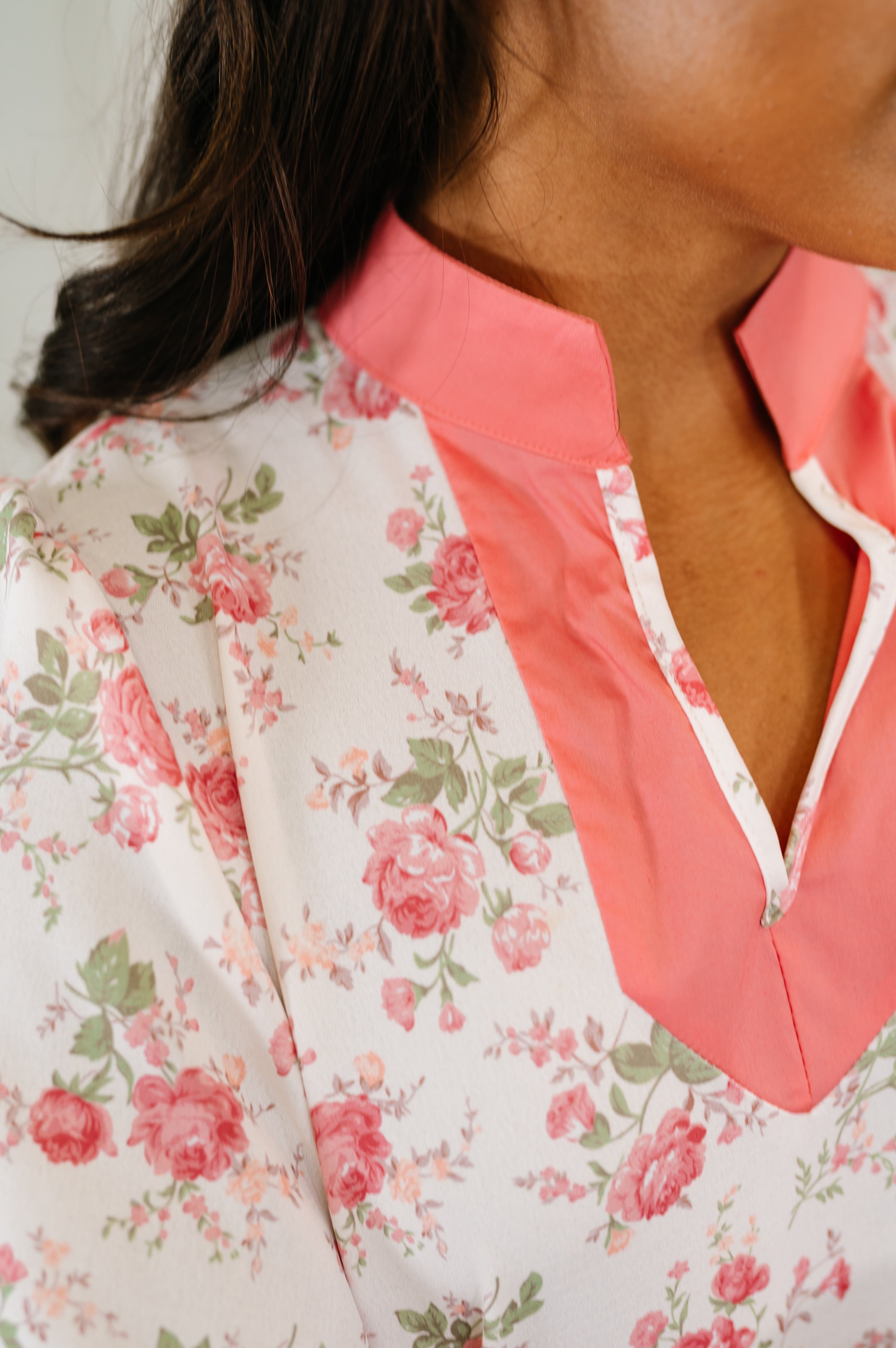 Close-up of floral blouse with coral split neck and green leaves in a bright, eclectic spring style setting