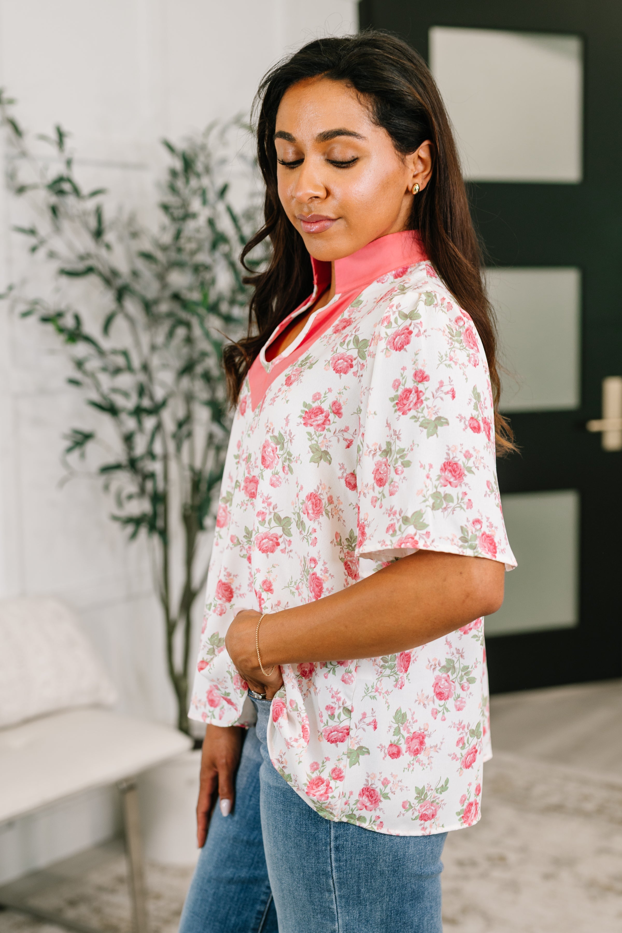 Woman wearing a floral blouse with coral split neck and relaxed sleeves in a bright, free-spirited indoor setting