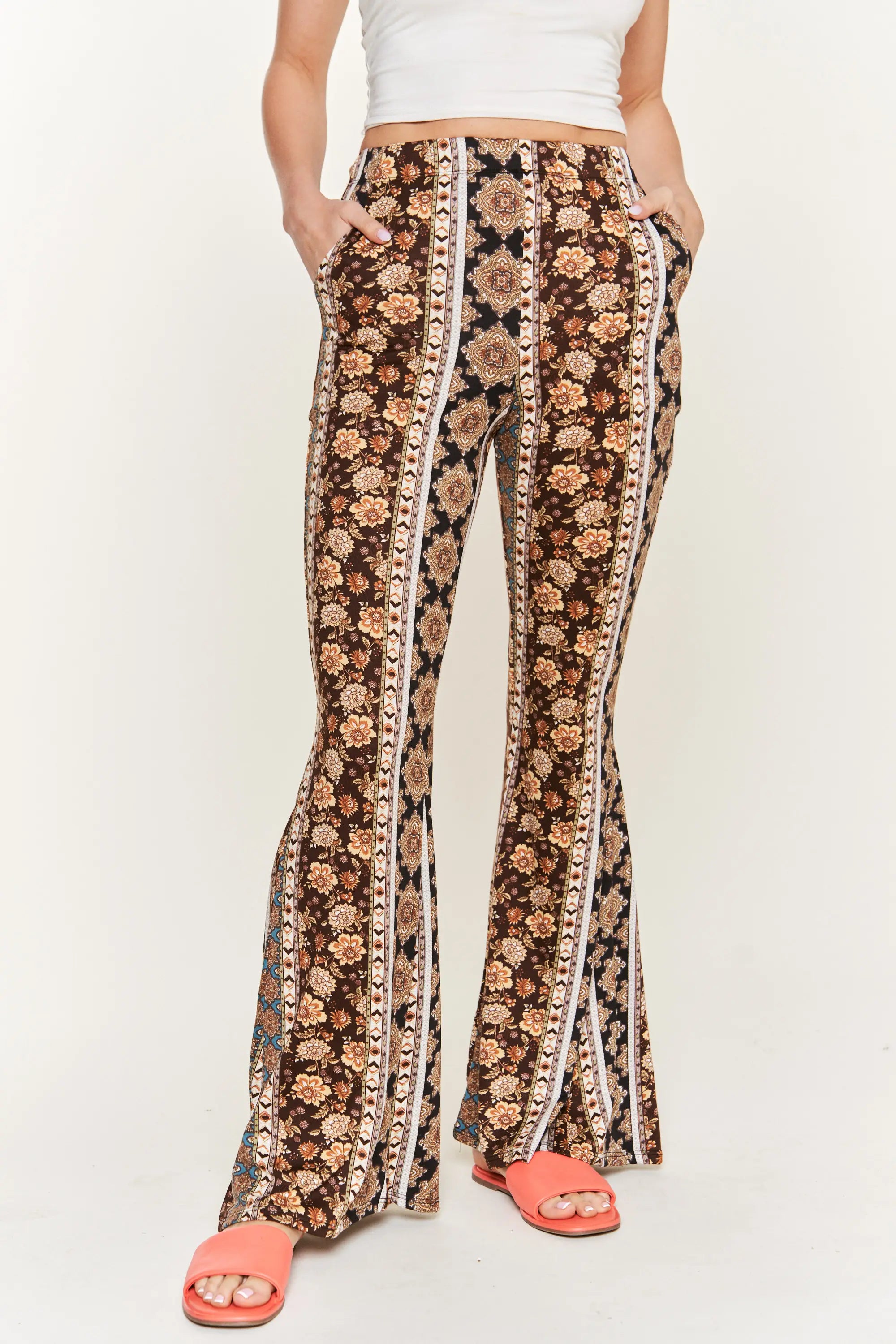 Front view of woman wearing high-waisted floral patterned flared pants with pockets and coral slide sandals