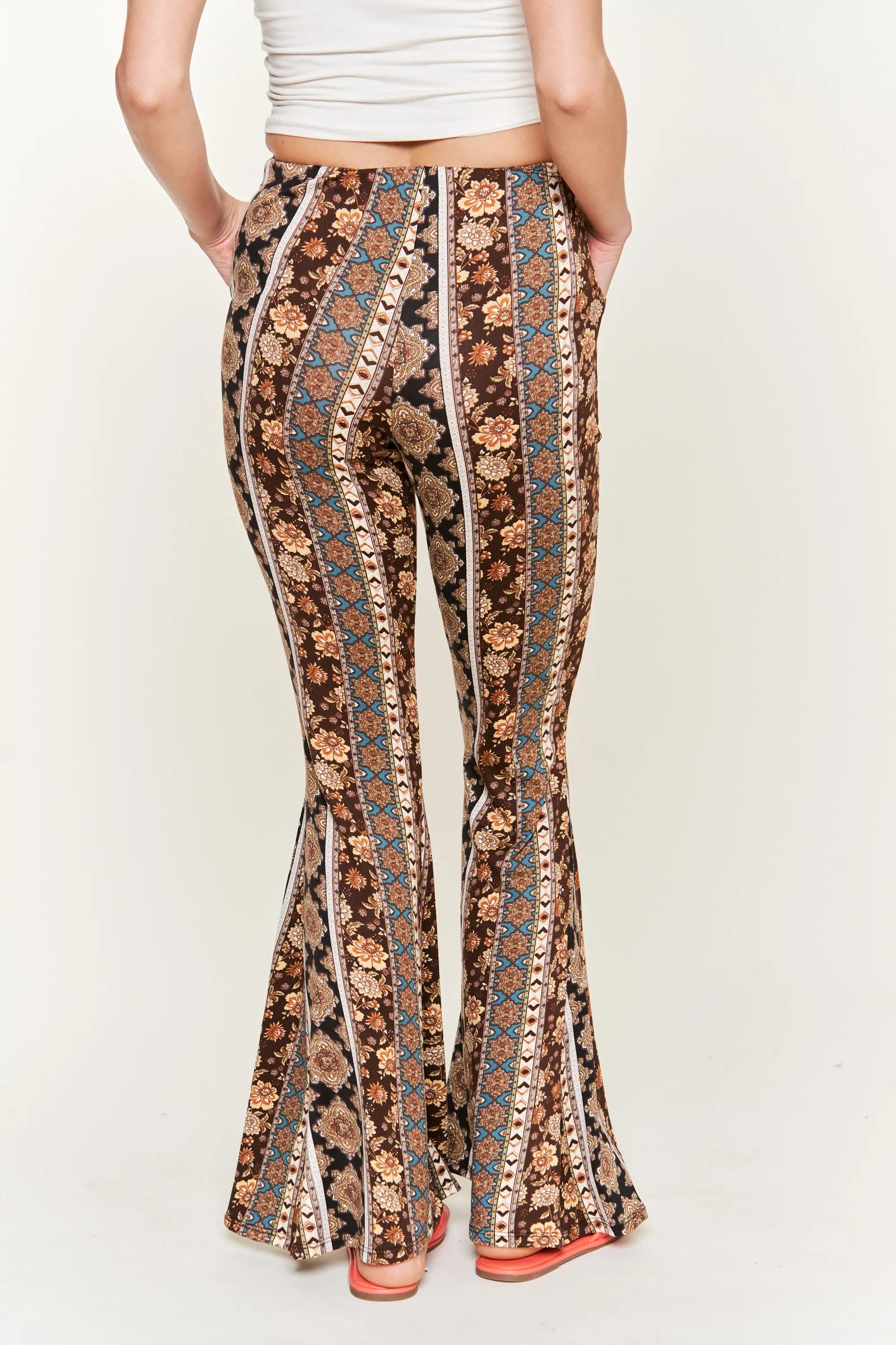 Rear view of woman wearing high-waisted floral patterned flared pants with pockets and a white crop top