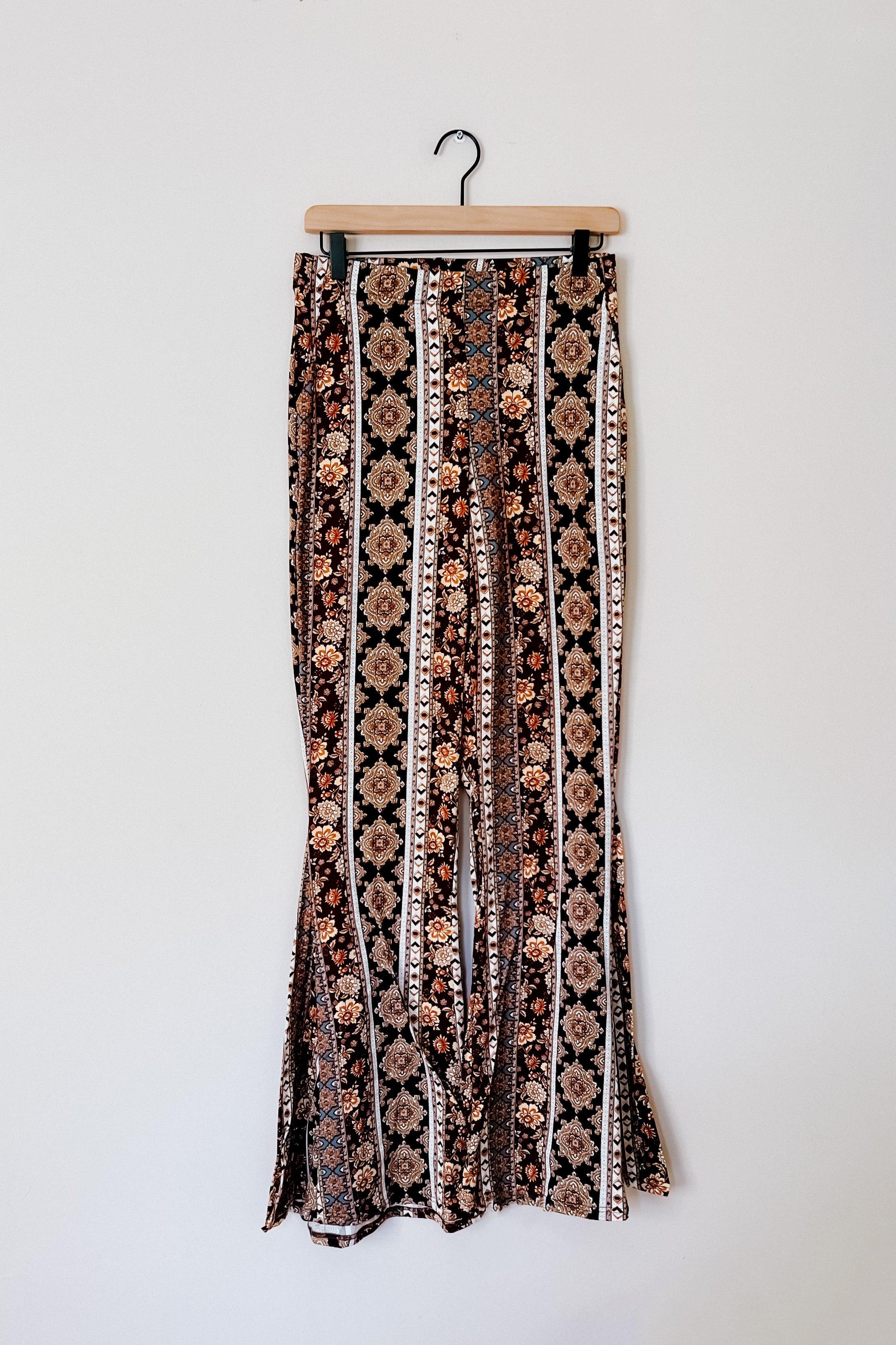 Floral and geometric patterned flared pants hanging on wooden hanger against white wall background