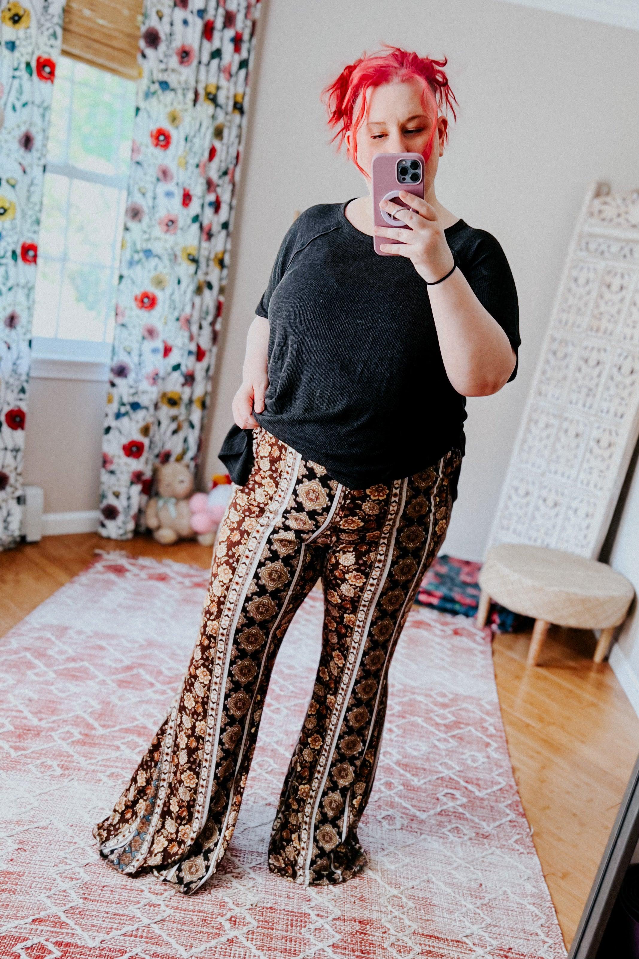 Woman taking mirror selfie wearing floral patterned flared pants with vertical stripe designs in cozy room