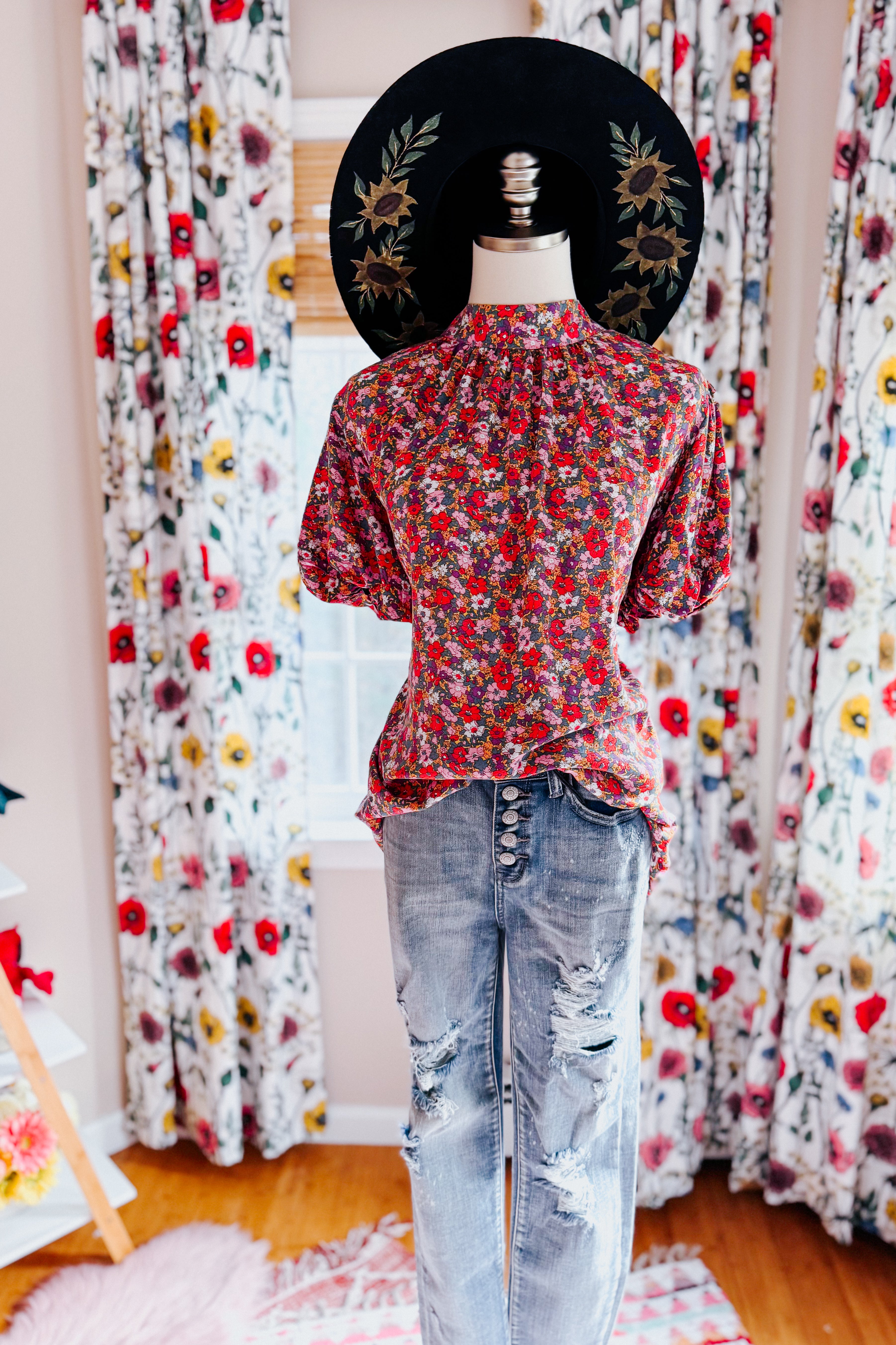 Mannequin dressed in red and purple floral mock neck blouse paired with distressed button-fly jeans indoors