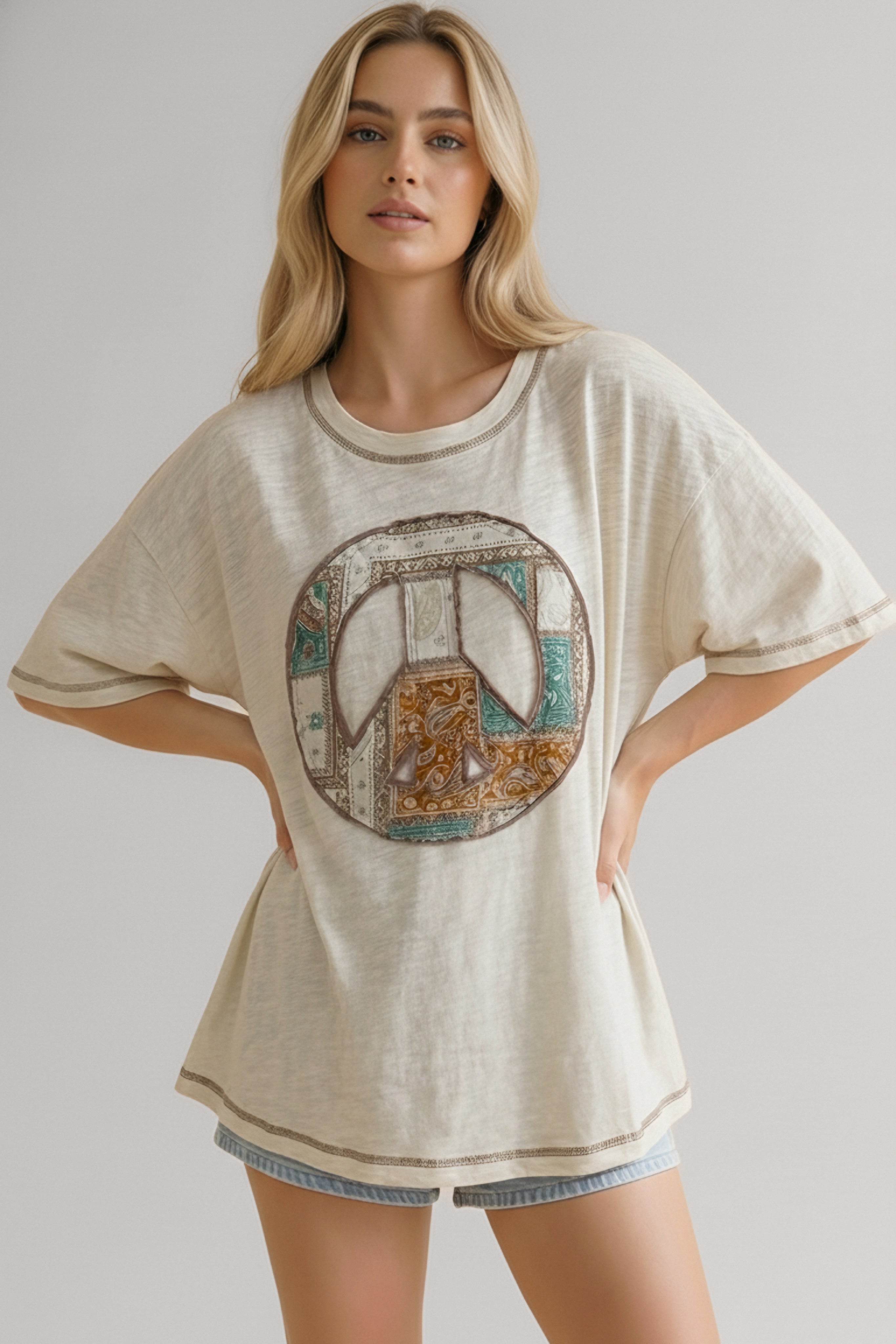 Woman wearing a cream short-sleeve tee with a patchwork peace sign graphic and light denim shorts