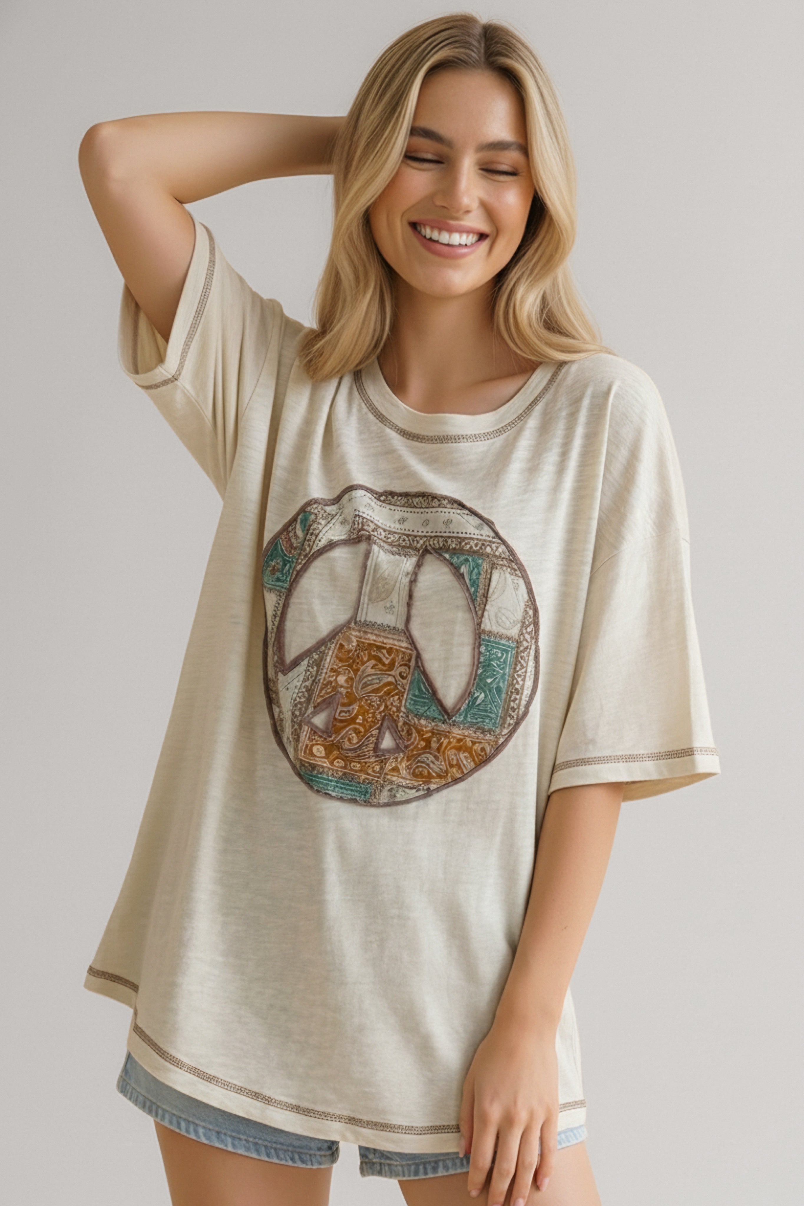 Smiling woman wearing a cream relaxed-fit tee with a multicolor peace sign graphic and light wash denim shorts