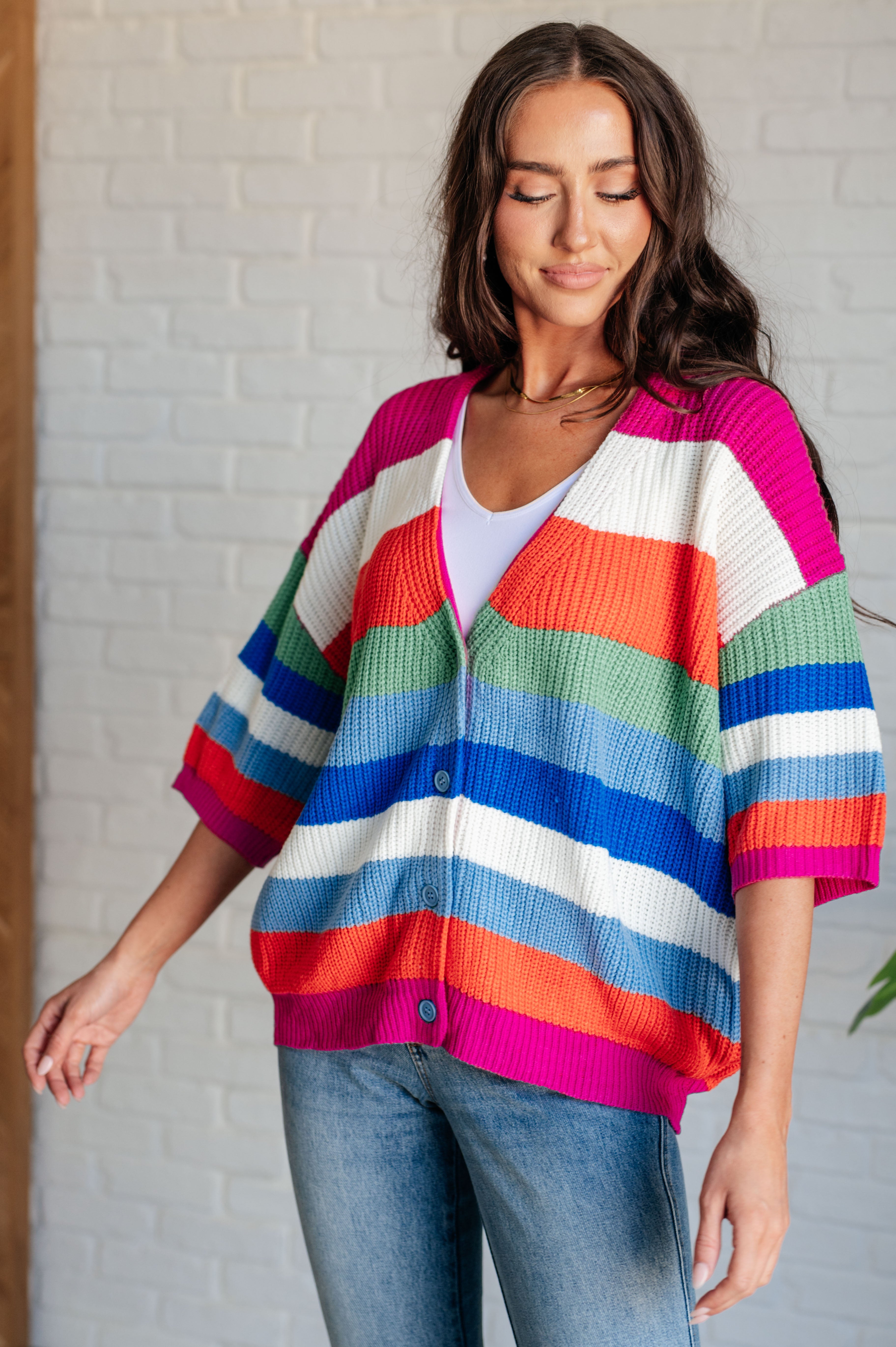 Woman wearing vibrant button-down cardigan with wide stripes in pink, orange, green, blue, and white over white top and jeans