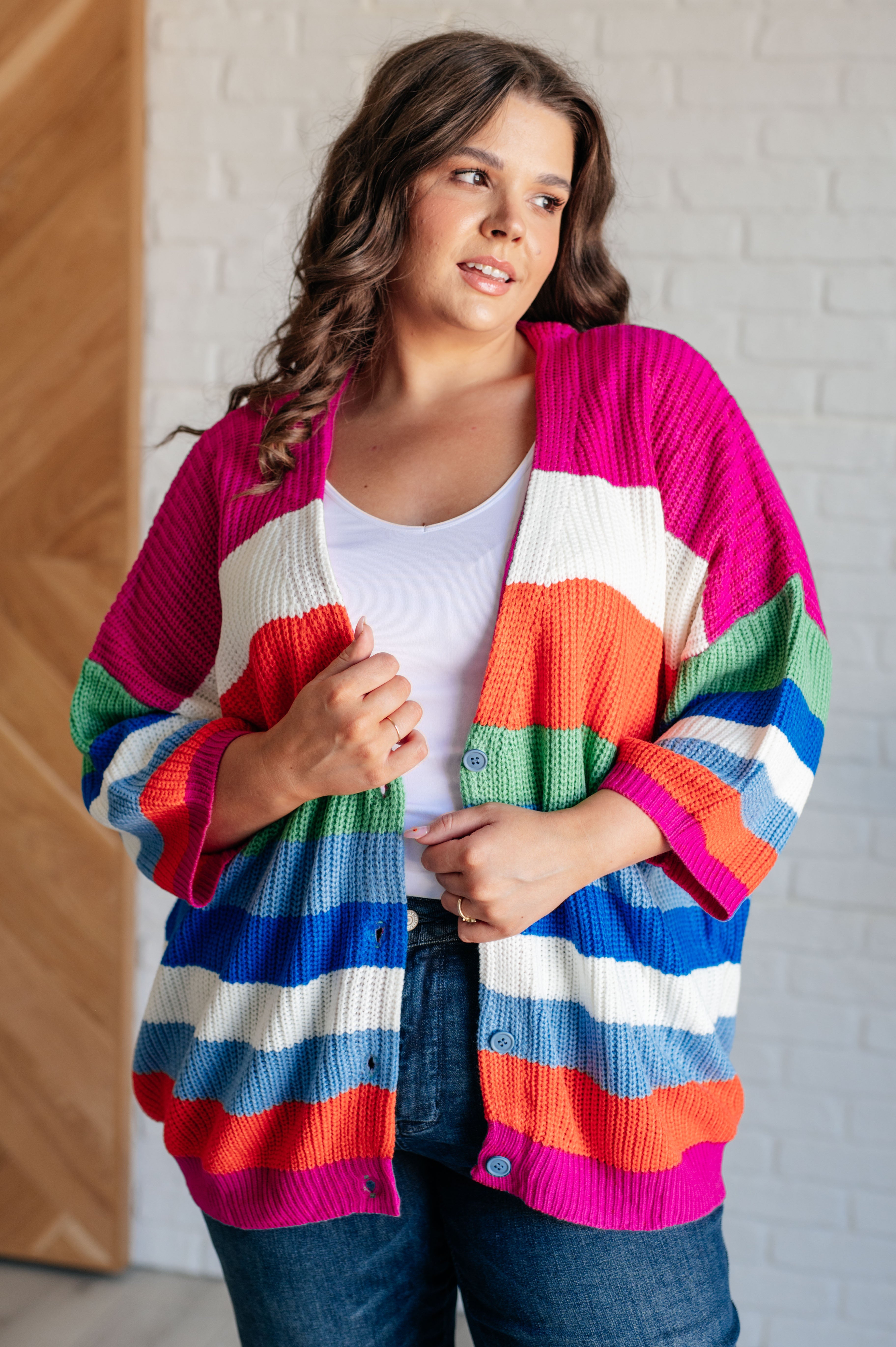 Plus size model wearing bold striped button-down cardigan with wide colorful stripes in pink, orange, green, blue, and white