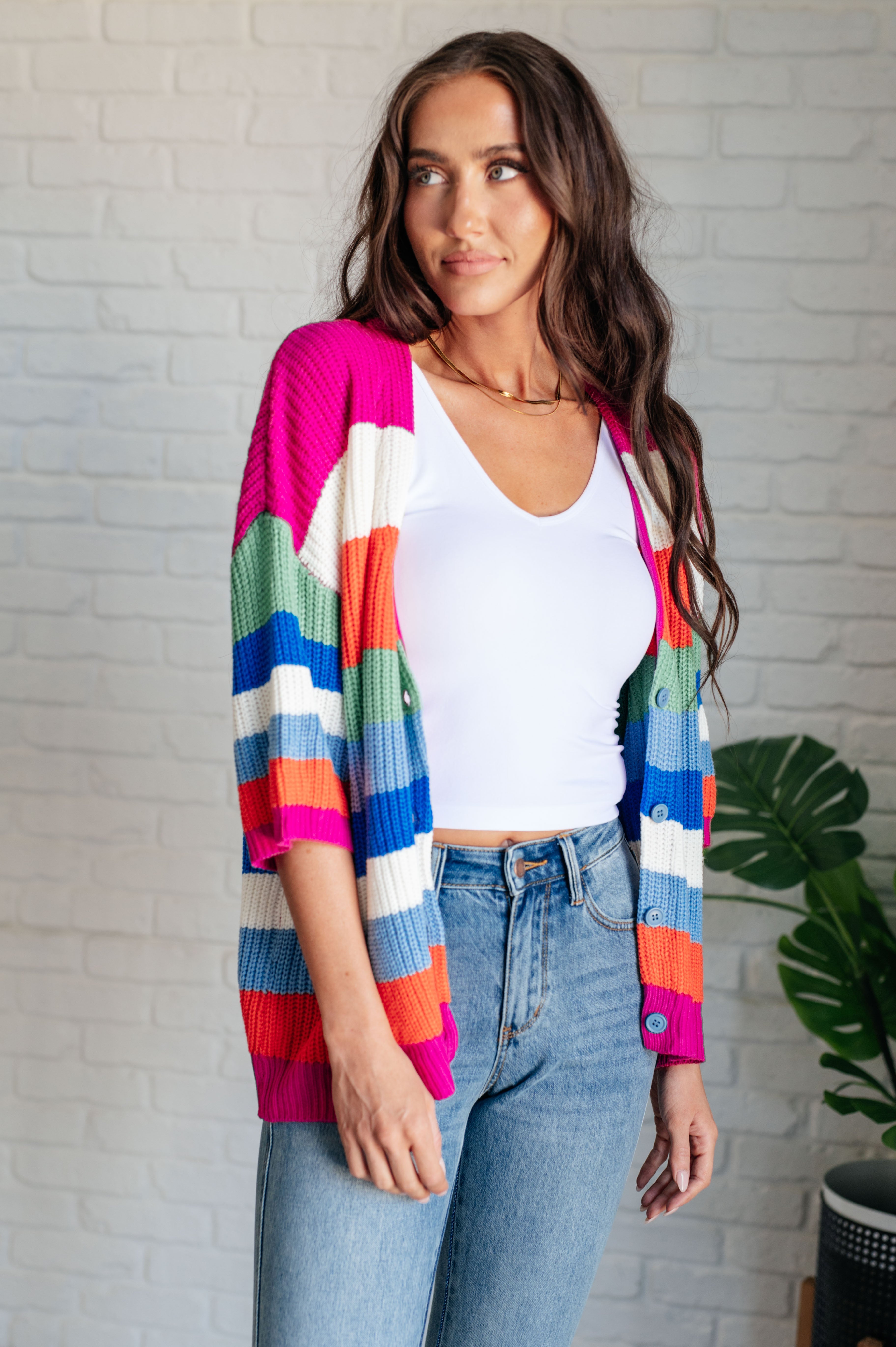 Woman wearing vibrant striped button-up cardigan with pink, orange, blue, green, and white colors over white tank top and jeans