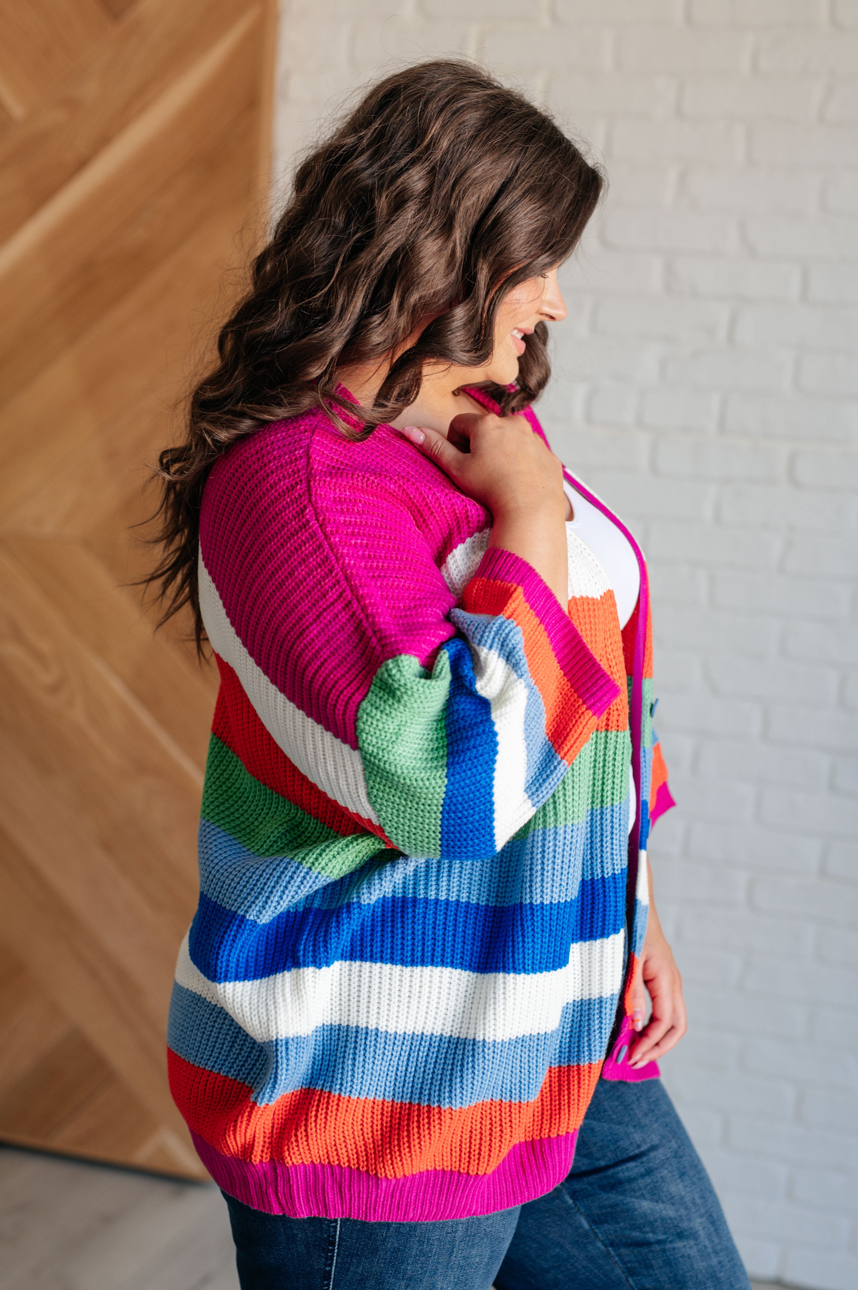 Side view of woman wearing bold multicolor striped chunky knit cardigan with vibrant pink, blue, green, and orange tones