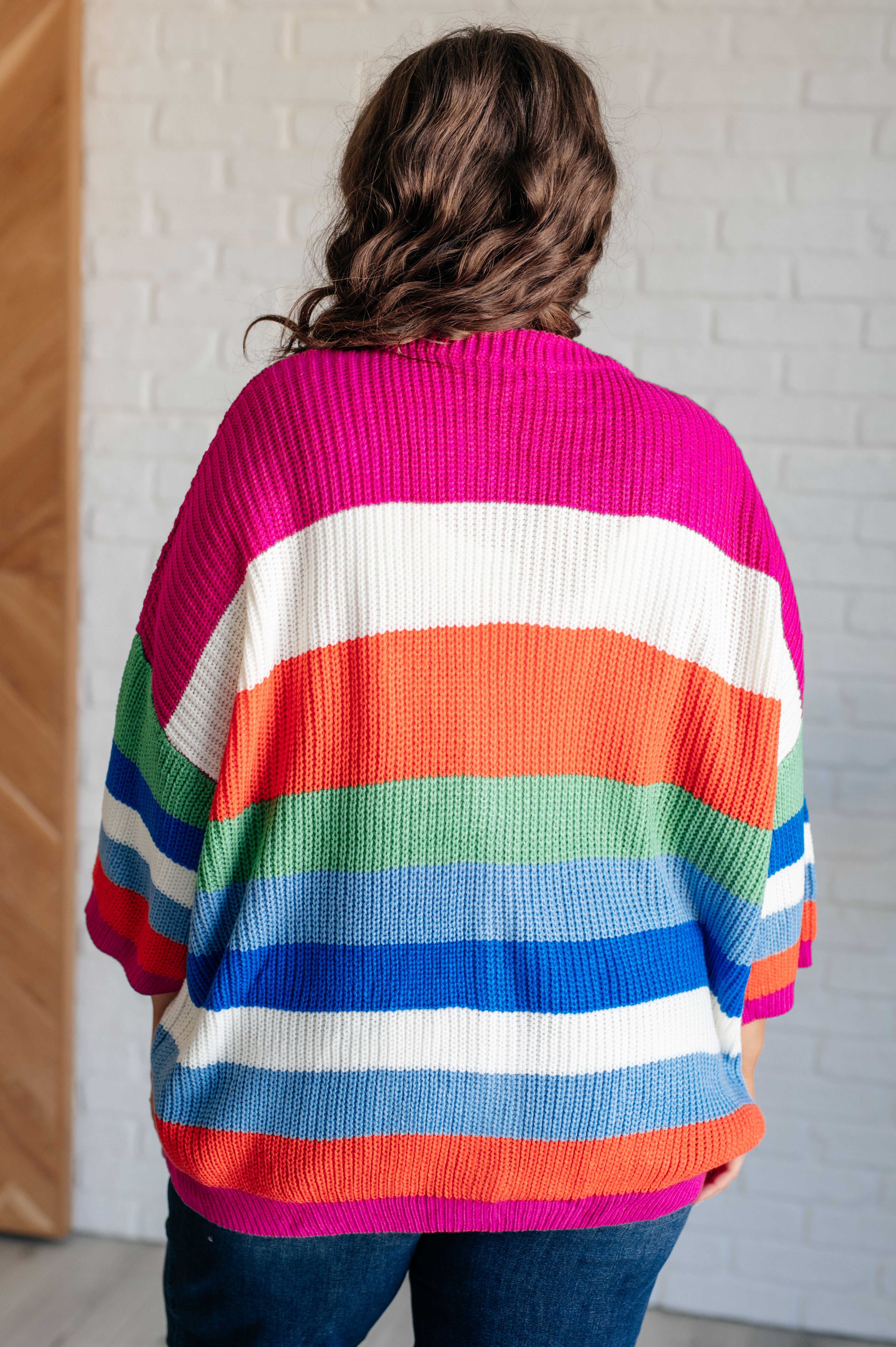 Back view of person wearing chunky knit cardigan with wide horizontal stripes in pink, white, orange, green, blue, and red