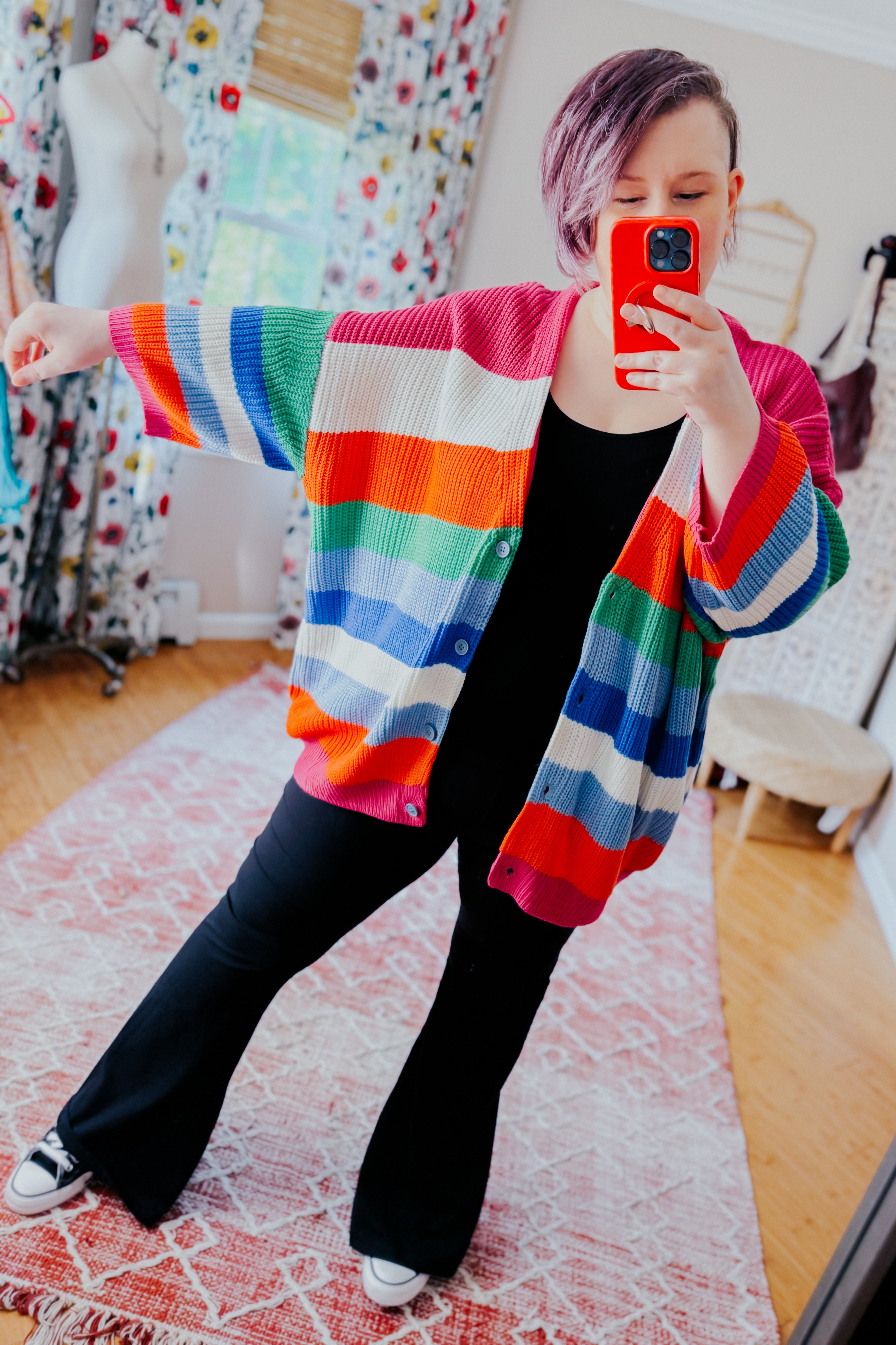 Woman with short hair taking mirror selfie wearing colorful striped bold button down cardigan with black outfit indoors