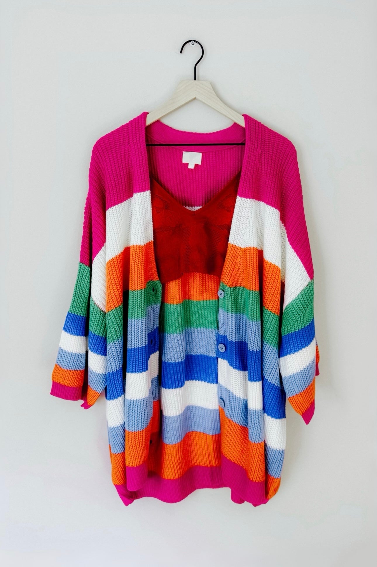 Vibrant oversized knit cardigan with bold multicolor horizontal stripes hanging on wooden hanger against white background