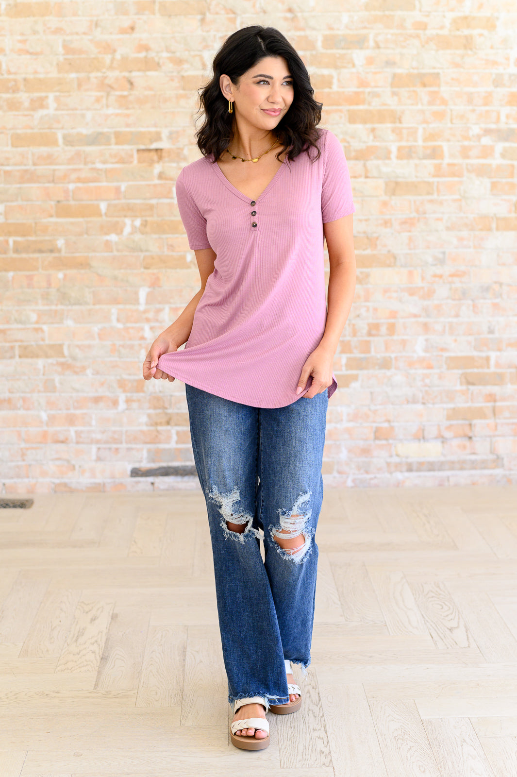 Woman wearing soft pink V-neck ribbed top with button detail paired with distressed blue jeans in bright indoor setting