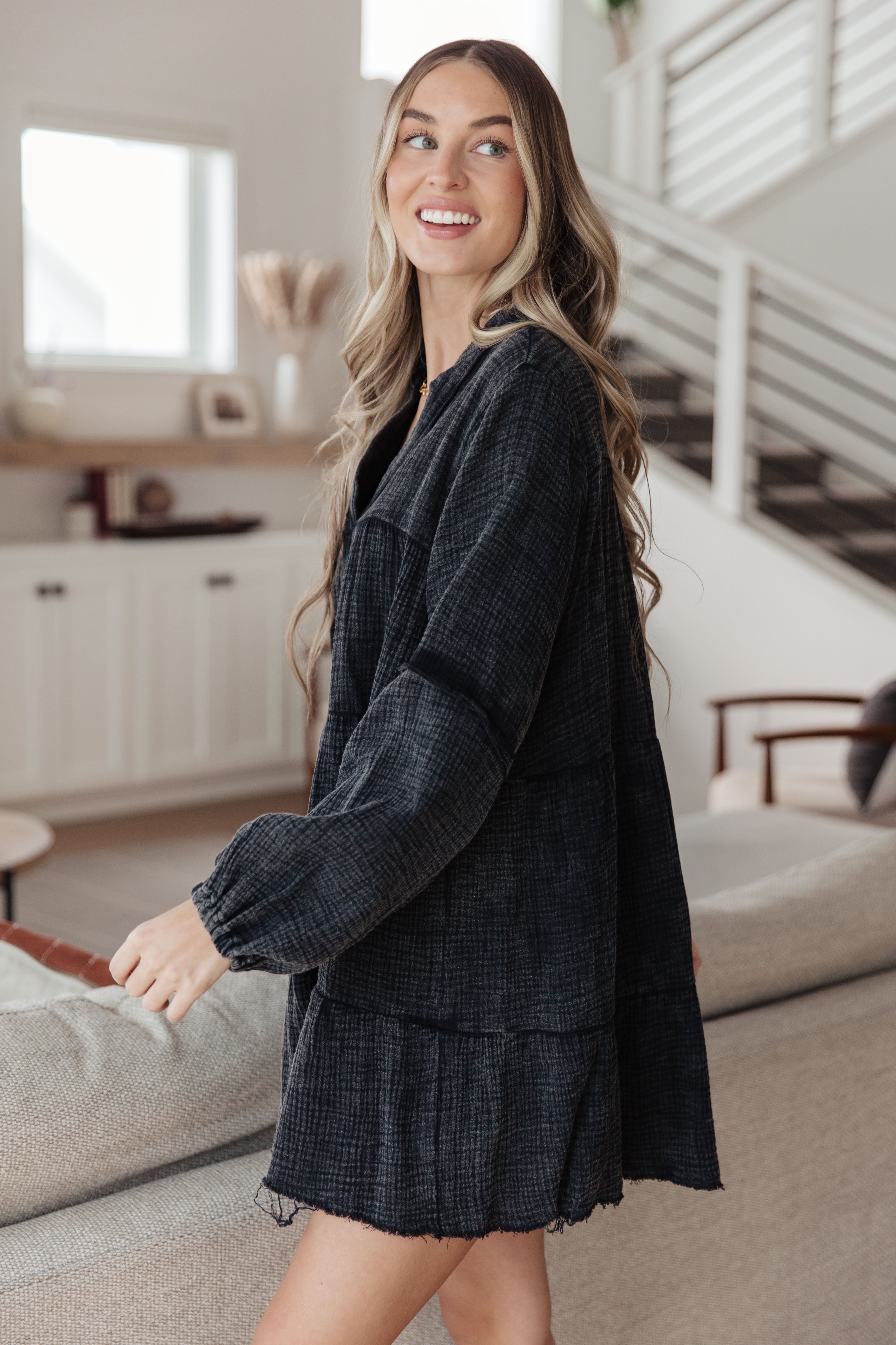 Woman wearing loose textured dark mineral wash dress with long gathered sleeves standing indoors smiling