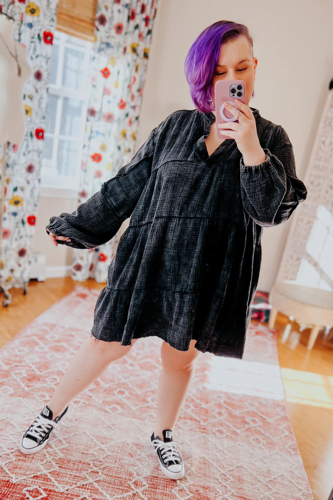 Woman with purple hair taking indoor mirror selfie wearing loose black mineral wash V-neck dress and black low-top sneakers