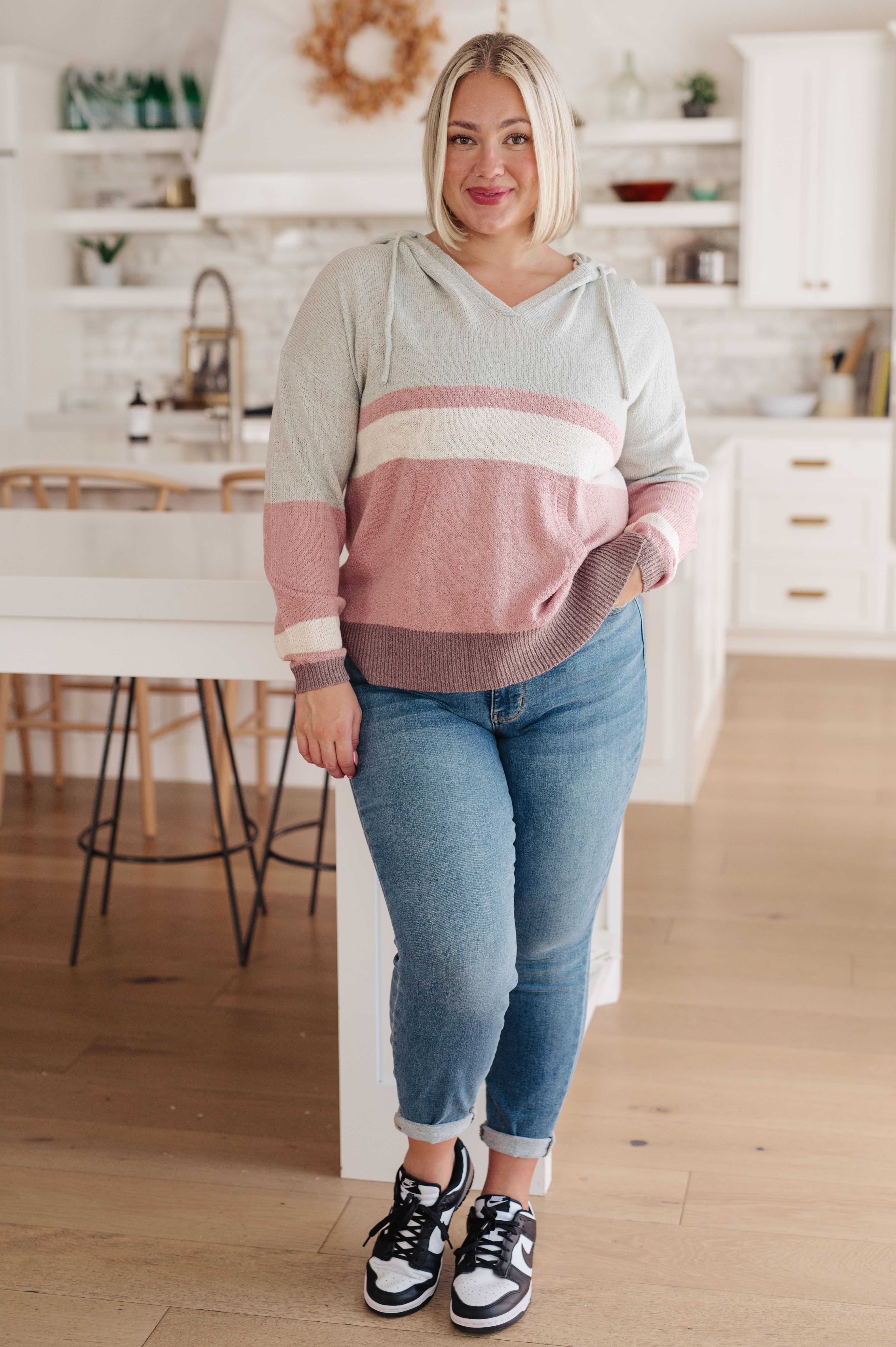 Blonde woman wearing pastel striped Boy Problem Spring Hoodie paired with cuffed jeans and black sneakers indoors