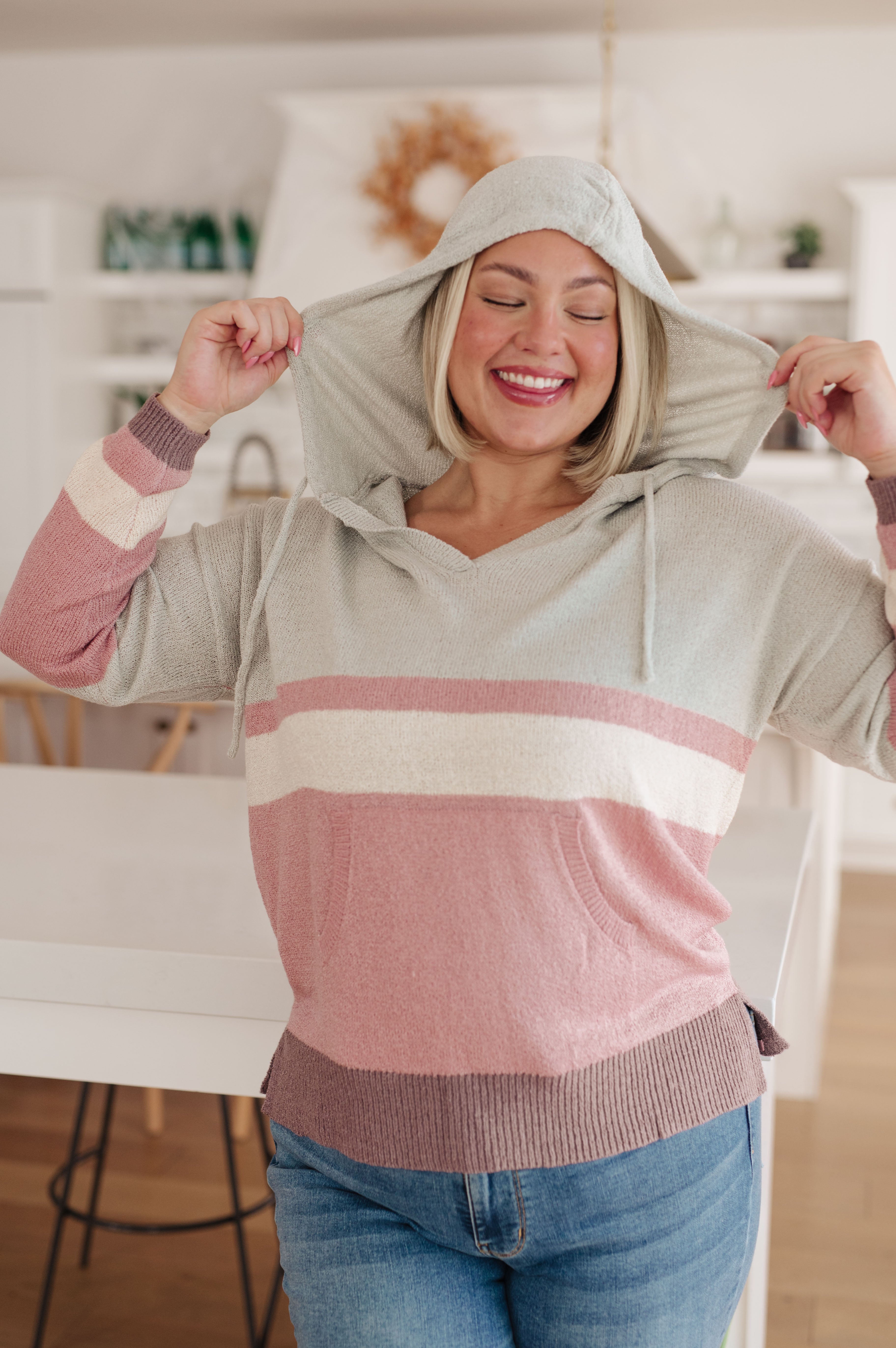 Woman with blonde bob wearing pastel striped Boy Problem Spring Hoodie smiling with hood up indoors
