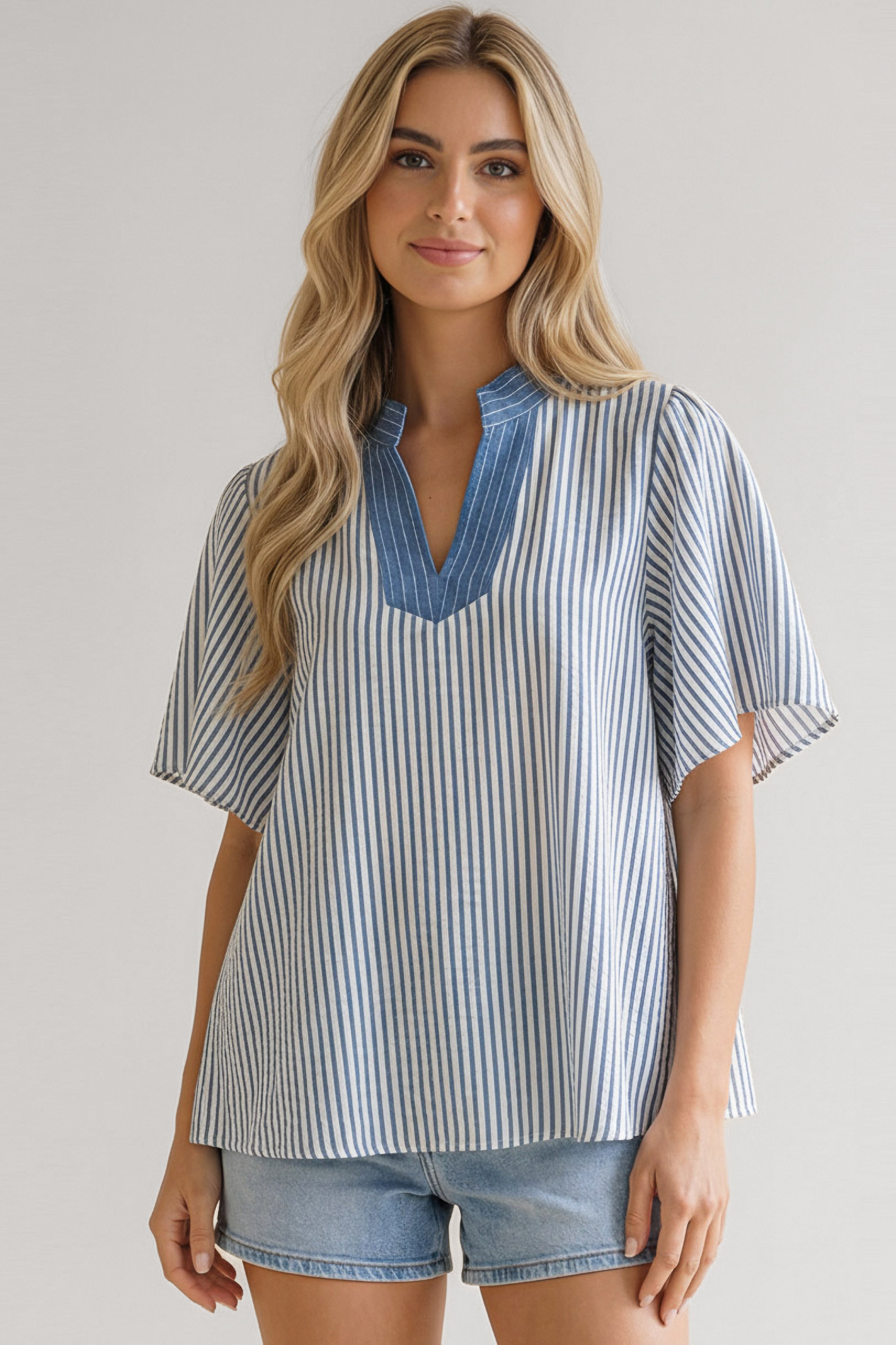 Young woman wearing blue striped loose top with V neckline and flutter sleeves paired with light blue denim shorts