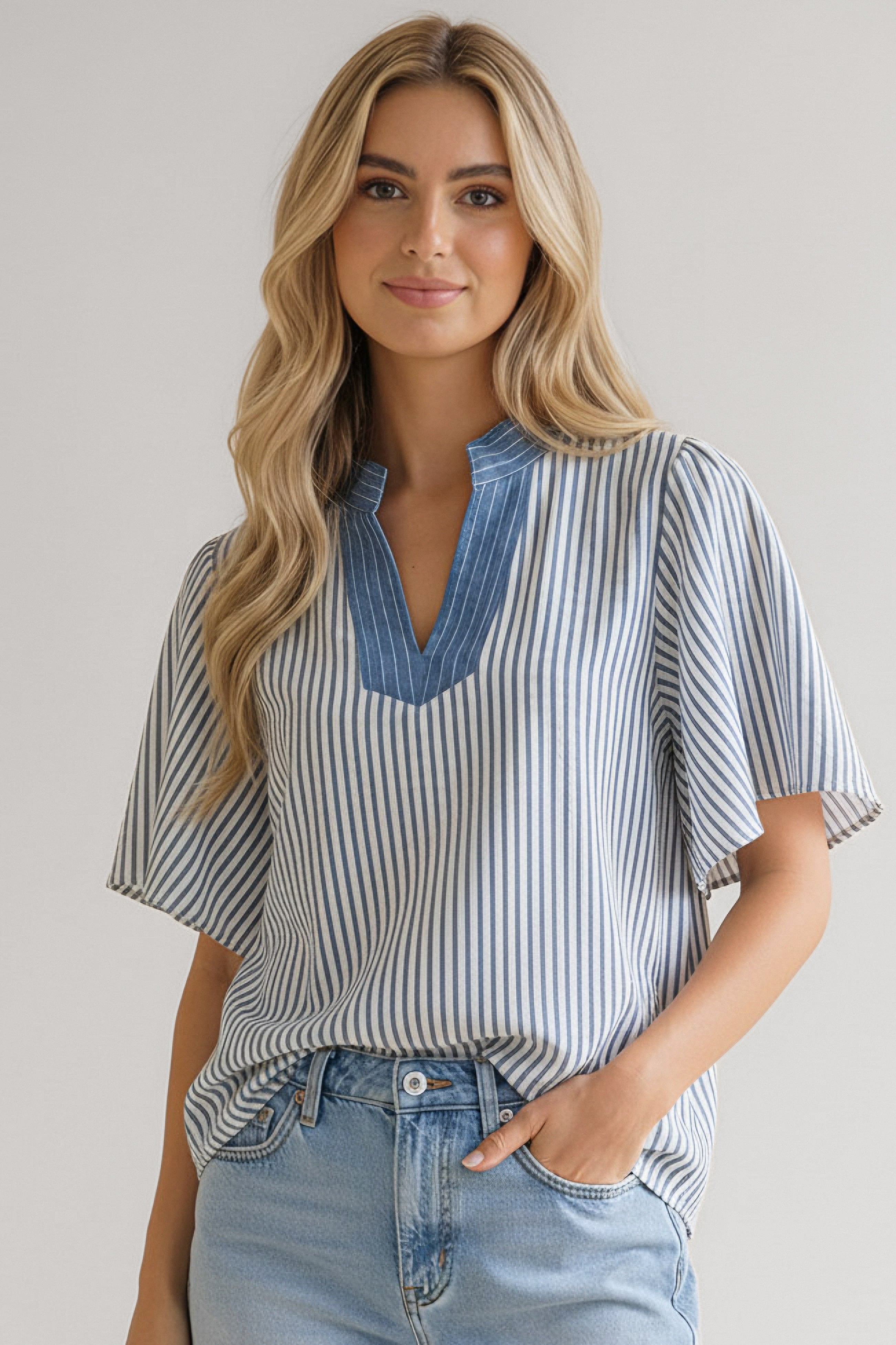 Woman wearing blue and white vertical striped blouse with flutter sleeves and contrasting blue neckline paired with light denim jeans