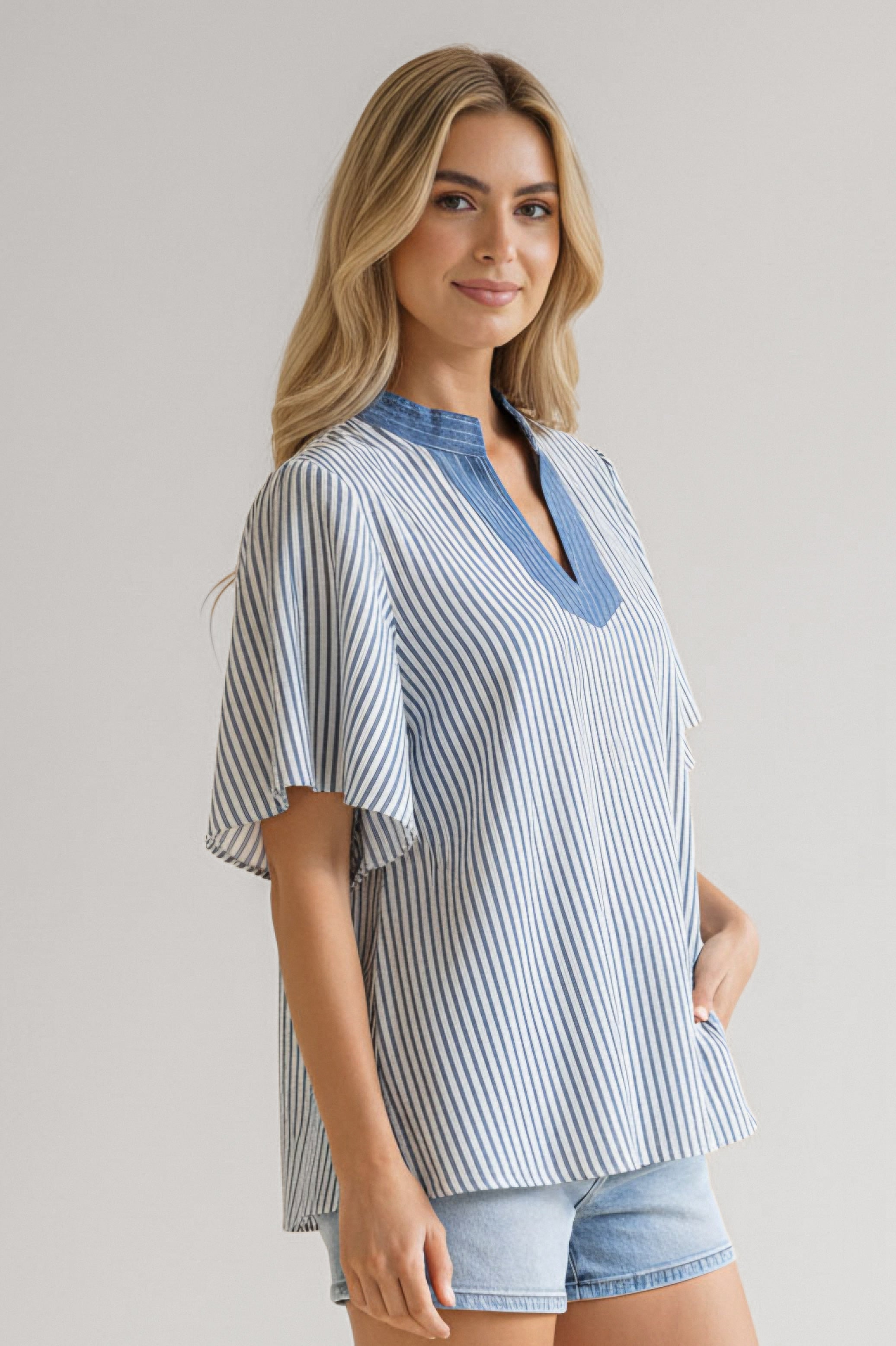 Woman wearing blue and white striped top with flutter sleeves and a blue contrasted neckline paired with light denim shorts