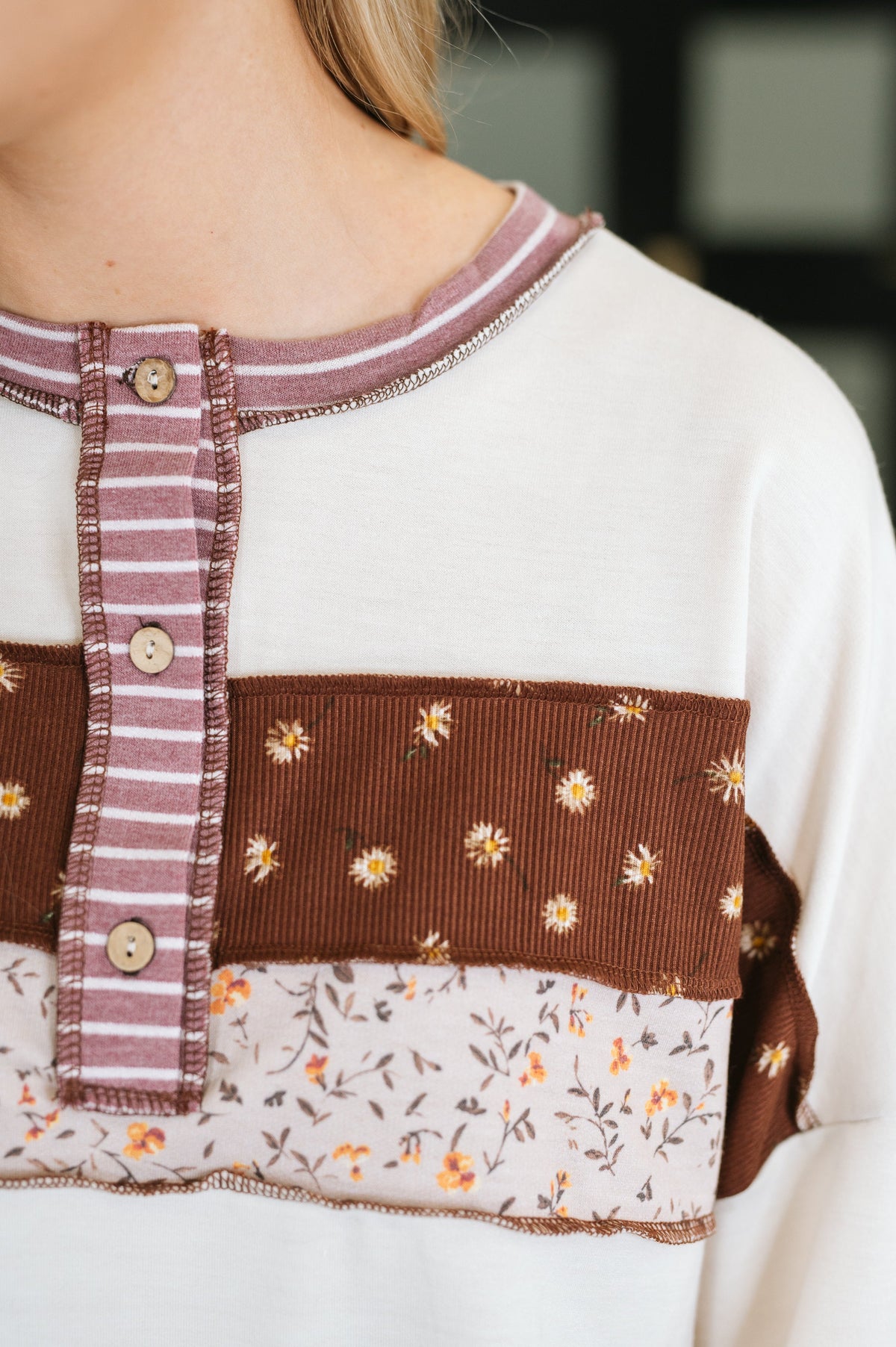 Close-up of a color block henley top with cream sleeves, rust floral panel, striped trim, and patterned hem detailing