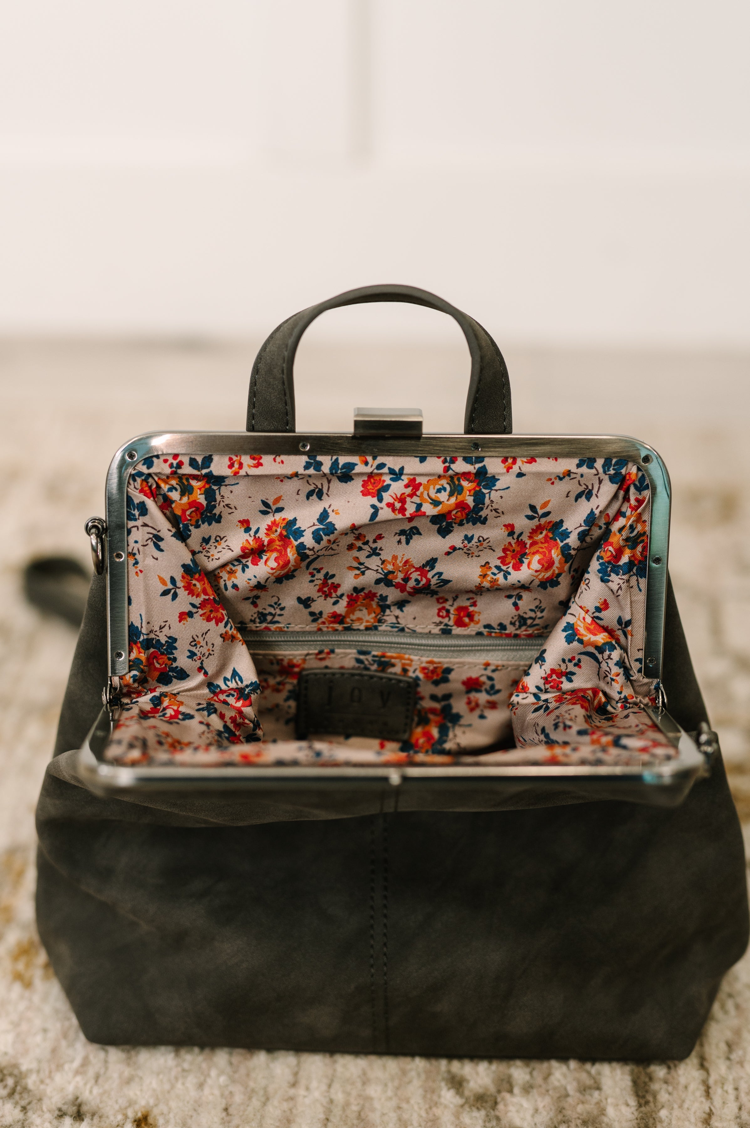 Open charcoal backpack featuring floral fabric lining and silver metal frame on textured surface