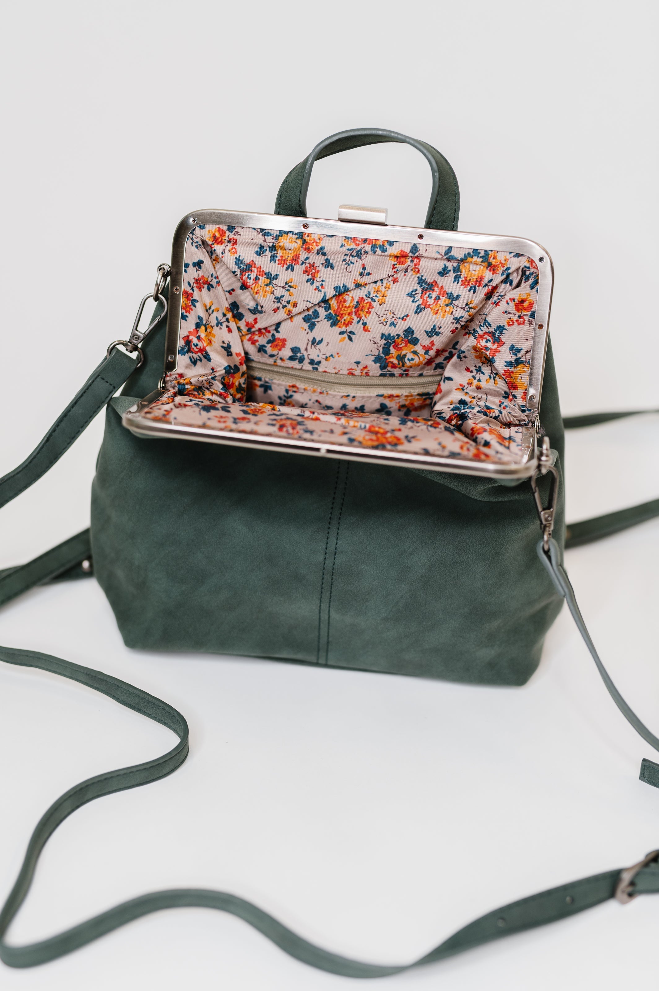 Small green backpack with floral fabric lining and metal frame clasp, displayed open on white background