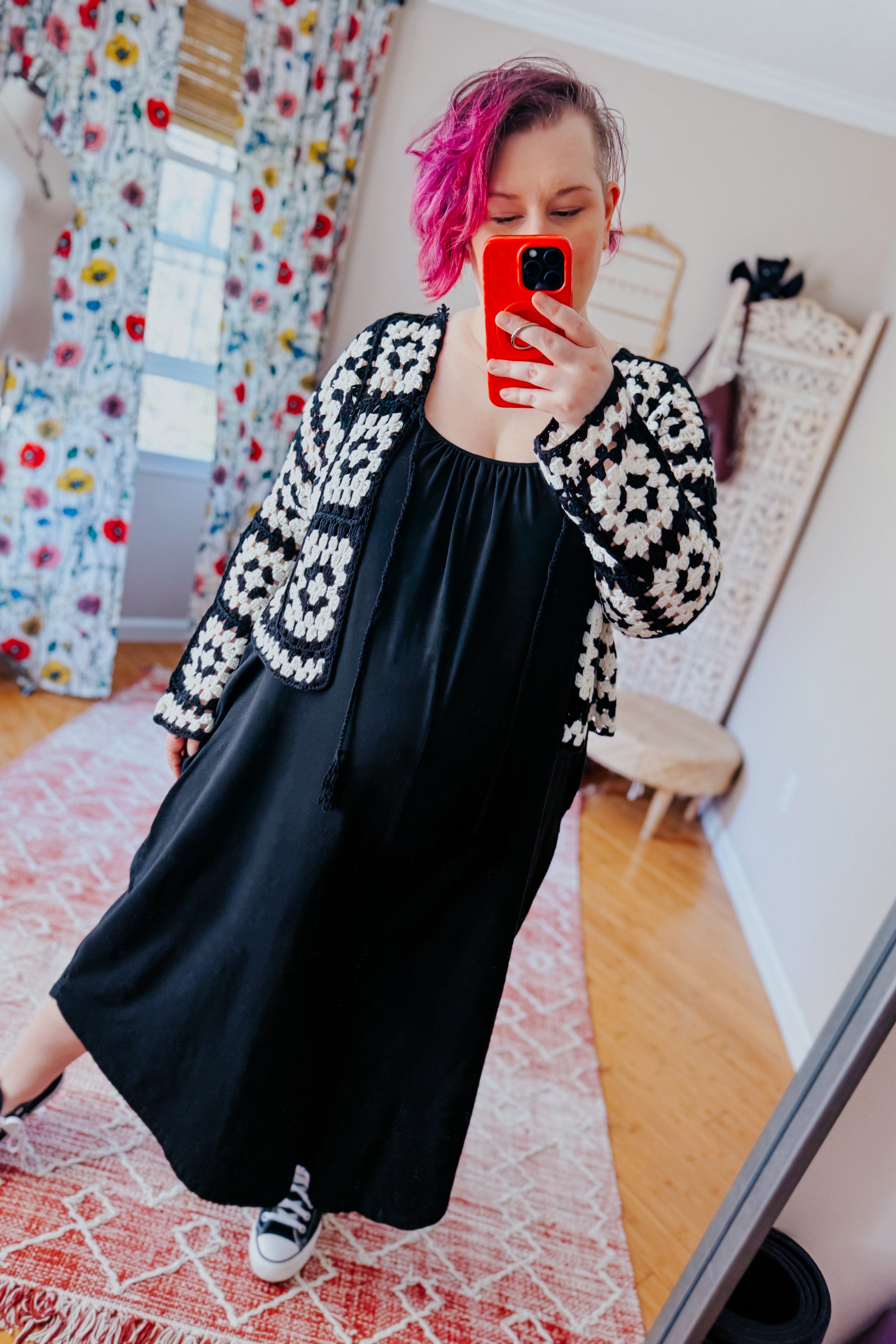 Woman taking selfie indoors wearing black dress with black and white crochet lightweight cropped cardigan and sneakers