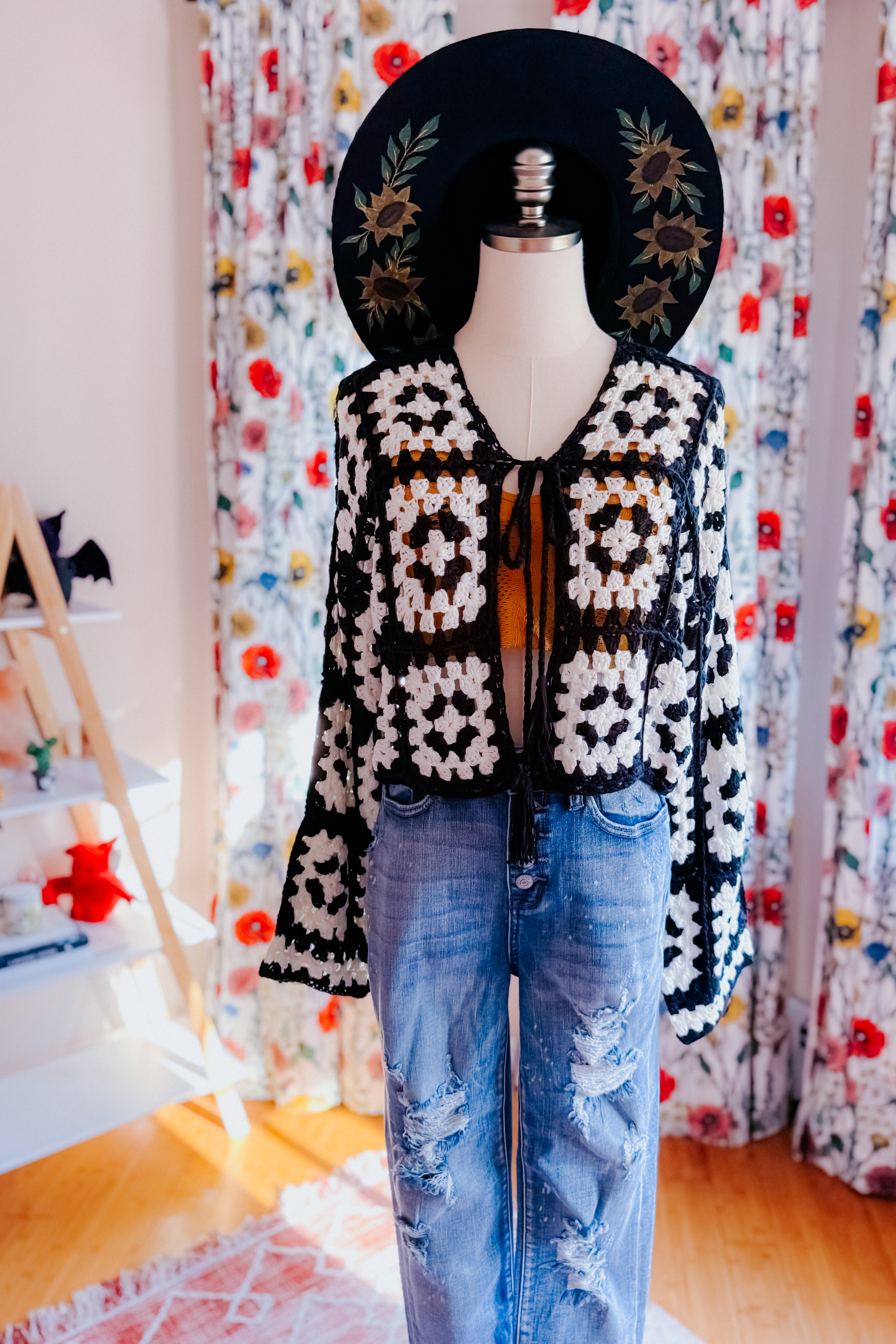 Black and white crochet cropped cardigan tied at front paired with distressed blue jeans on mannequin indoors