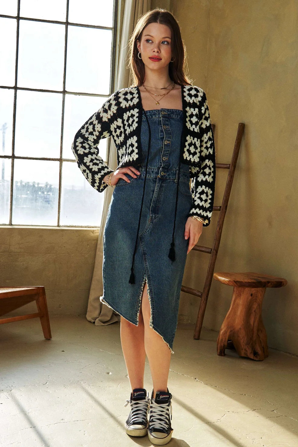 Woman posing indoors wearing black and white crochet cropped cardigan over sleeveless denim midi dress and sneakers