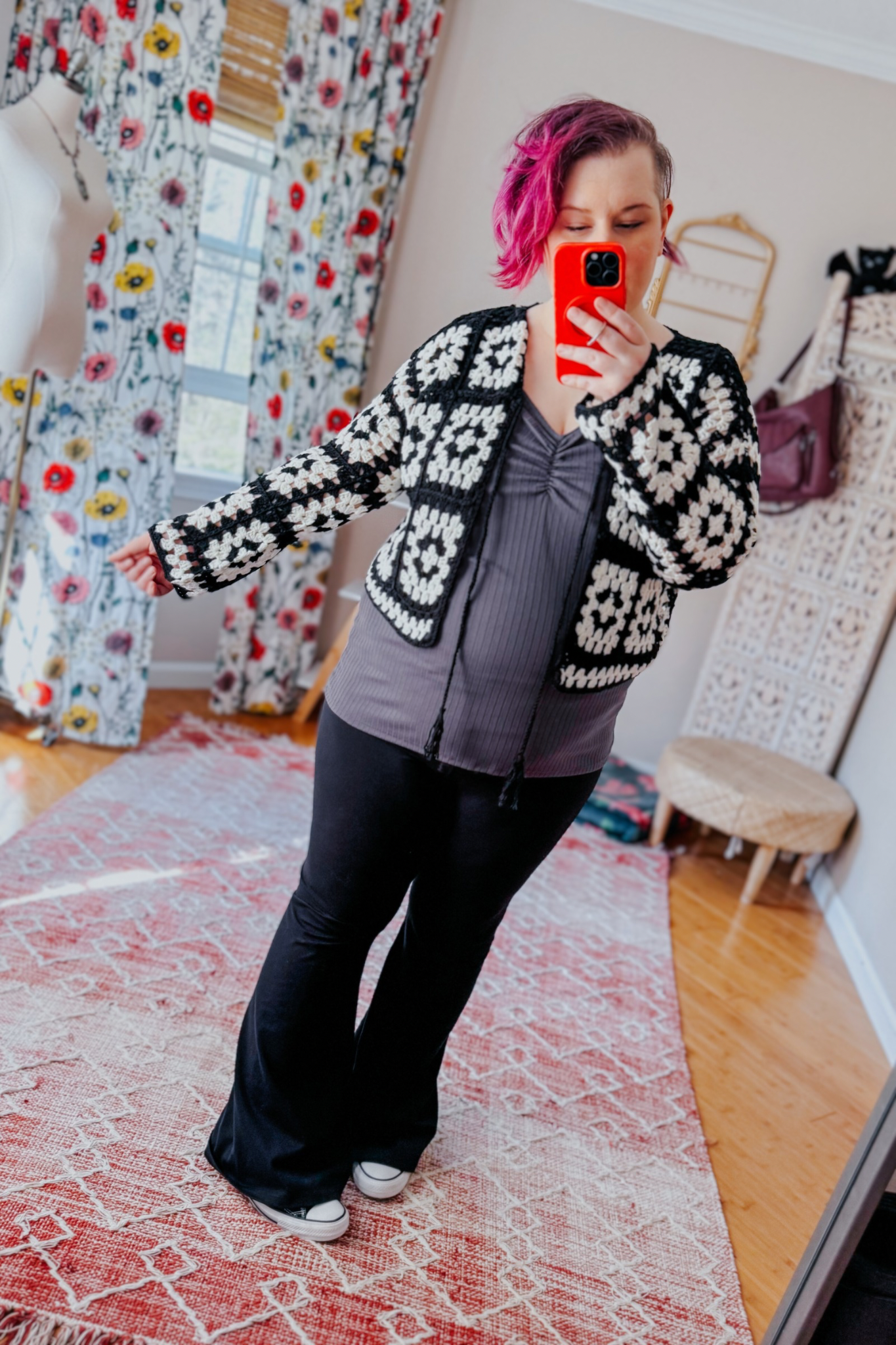 Person taking mirror selfie wearing black and white crochet cropped cardigan over gray ruched top and black pants indoors
