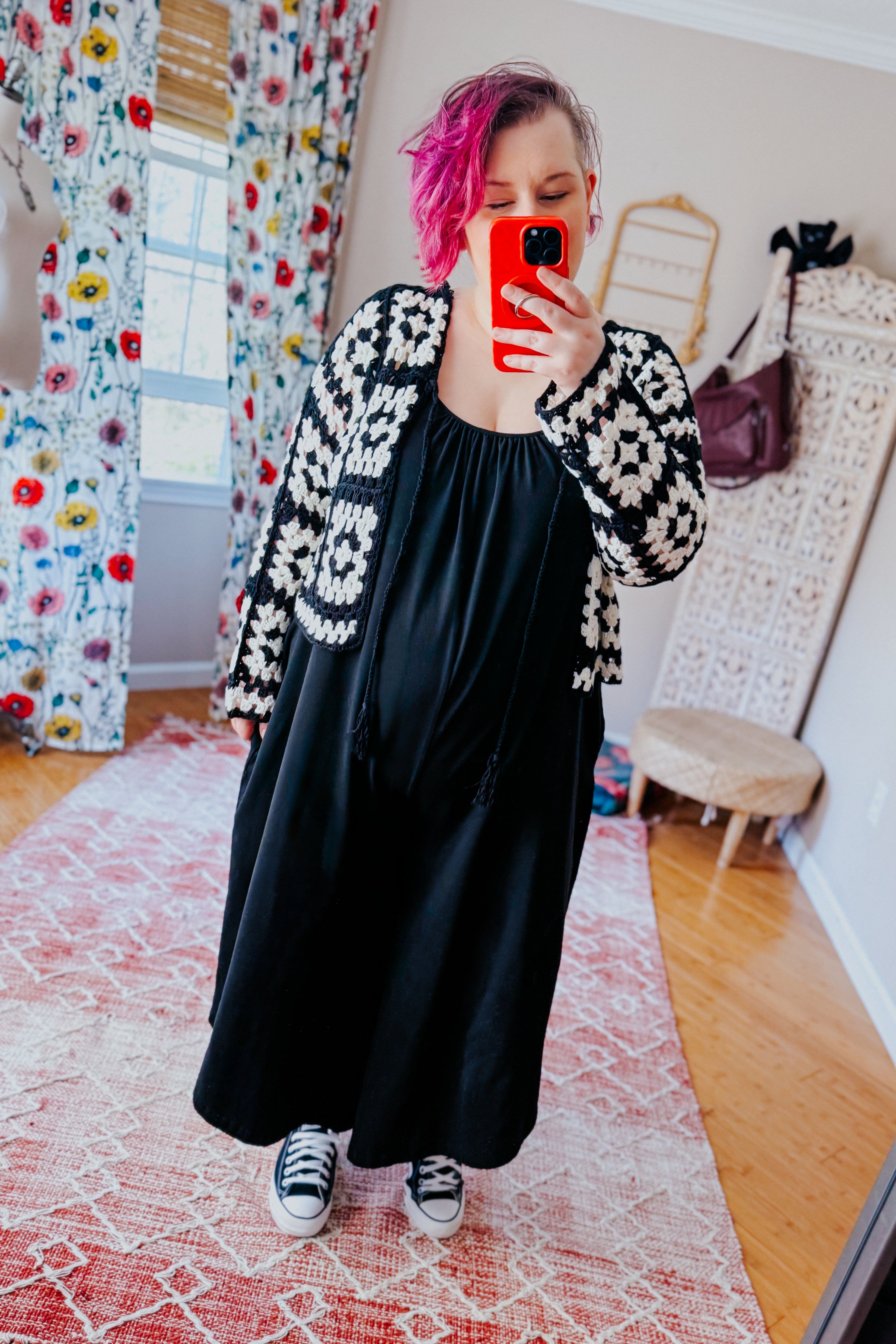 Woman taking indoor mirror selfie wearing black maxi dress with black and white crochet patterned cropped cardigan and sneakers