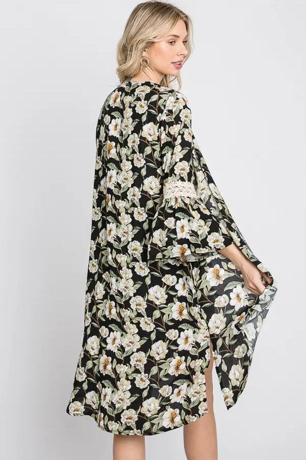 Blonde woman wearing black floral 3/4 bell sleeve duster with lace detail posing sideways against light background