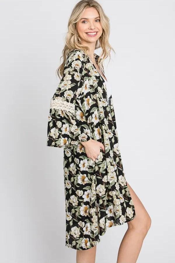 Smiling blonde woman in floral print 3/4 bell sleeve duster with lace detail posing against gray background