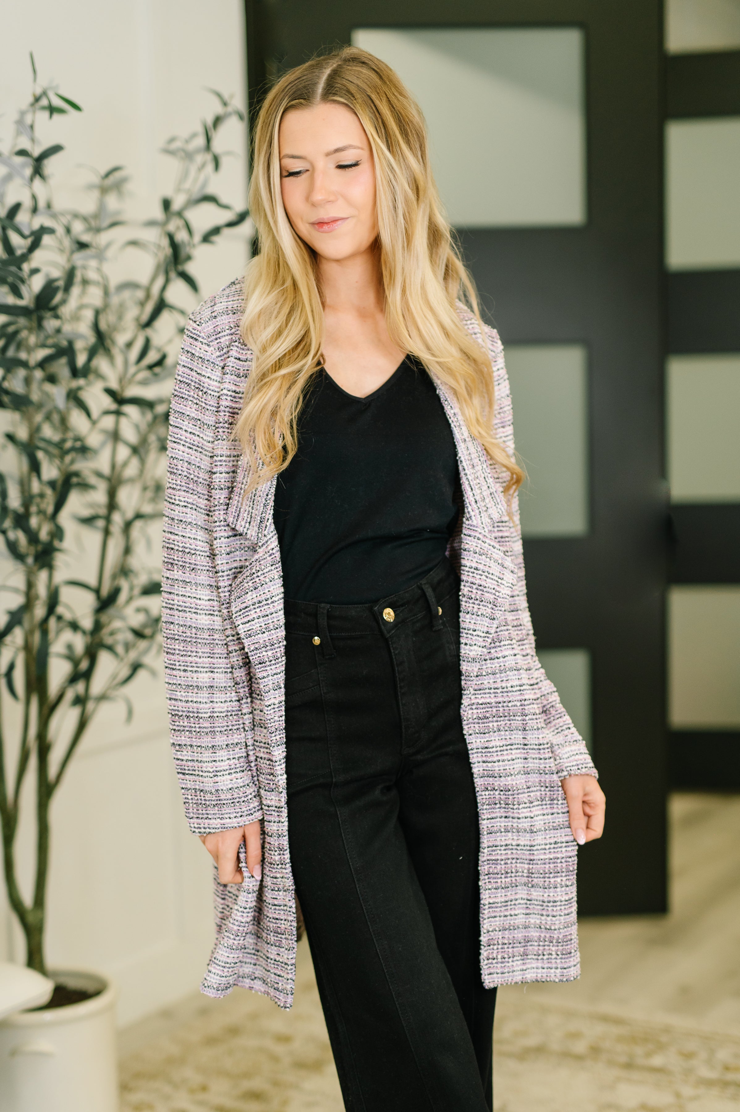 Young woman wearing a lavender ivory tweed blazer over black top and high-waisted black pants indoors